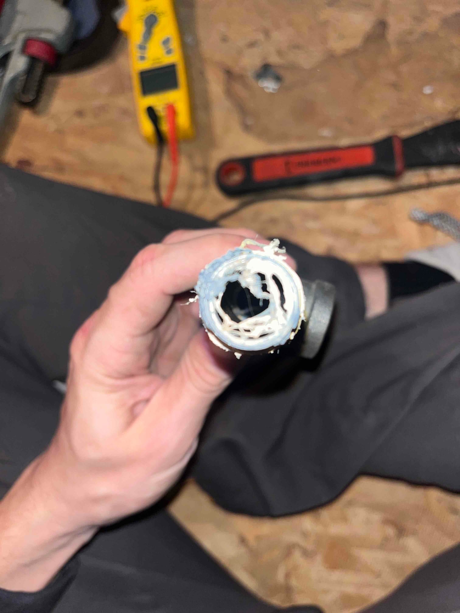Section of plastic drain tubing held open, showing significant white residue and debris inside the bore.