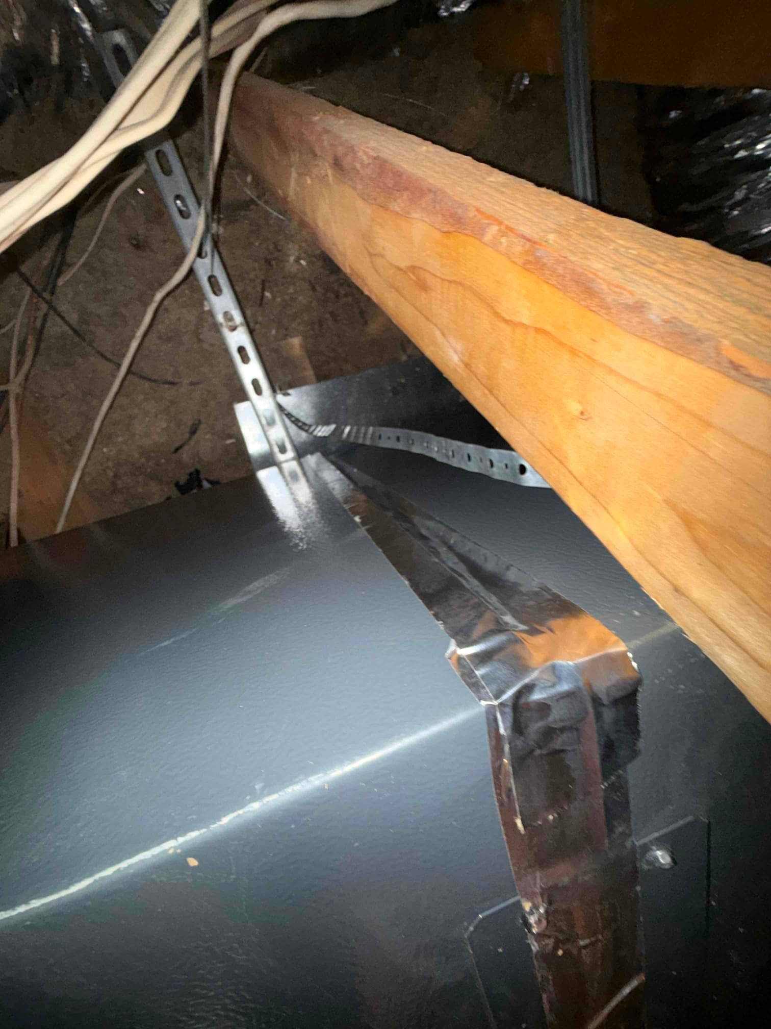 Sheet metal duct with foil tape along a seam, near attic joist and support strap.