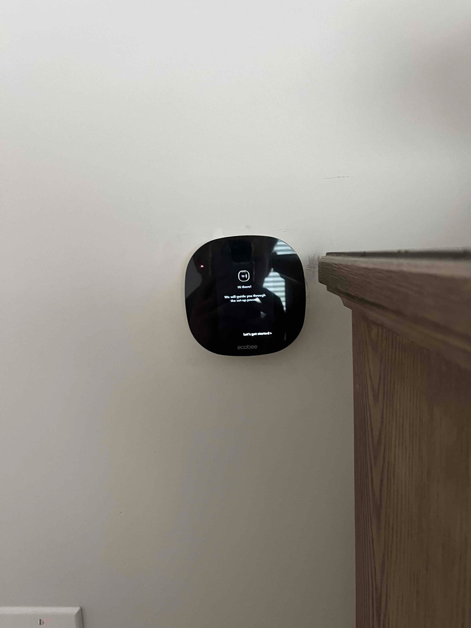 Smart thermostat mounted on an interior wall, display shows the on-screen setup instructions during installation.