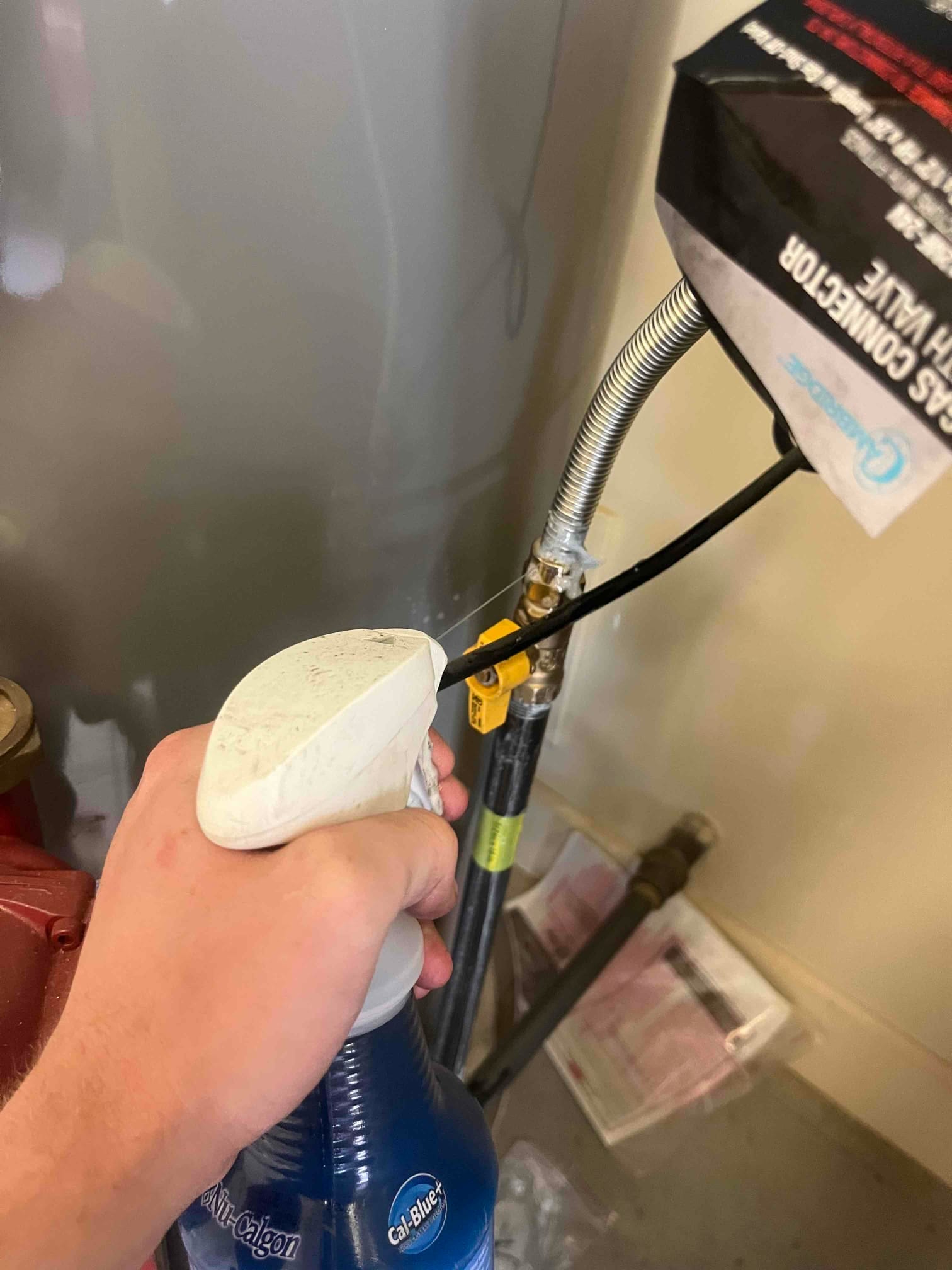 Technician applies leak detector solution to the gas shutoff valve and flexible connector at the appliance.