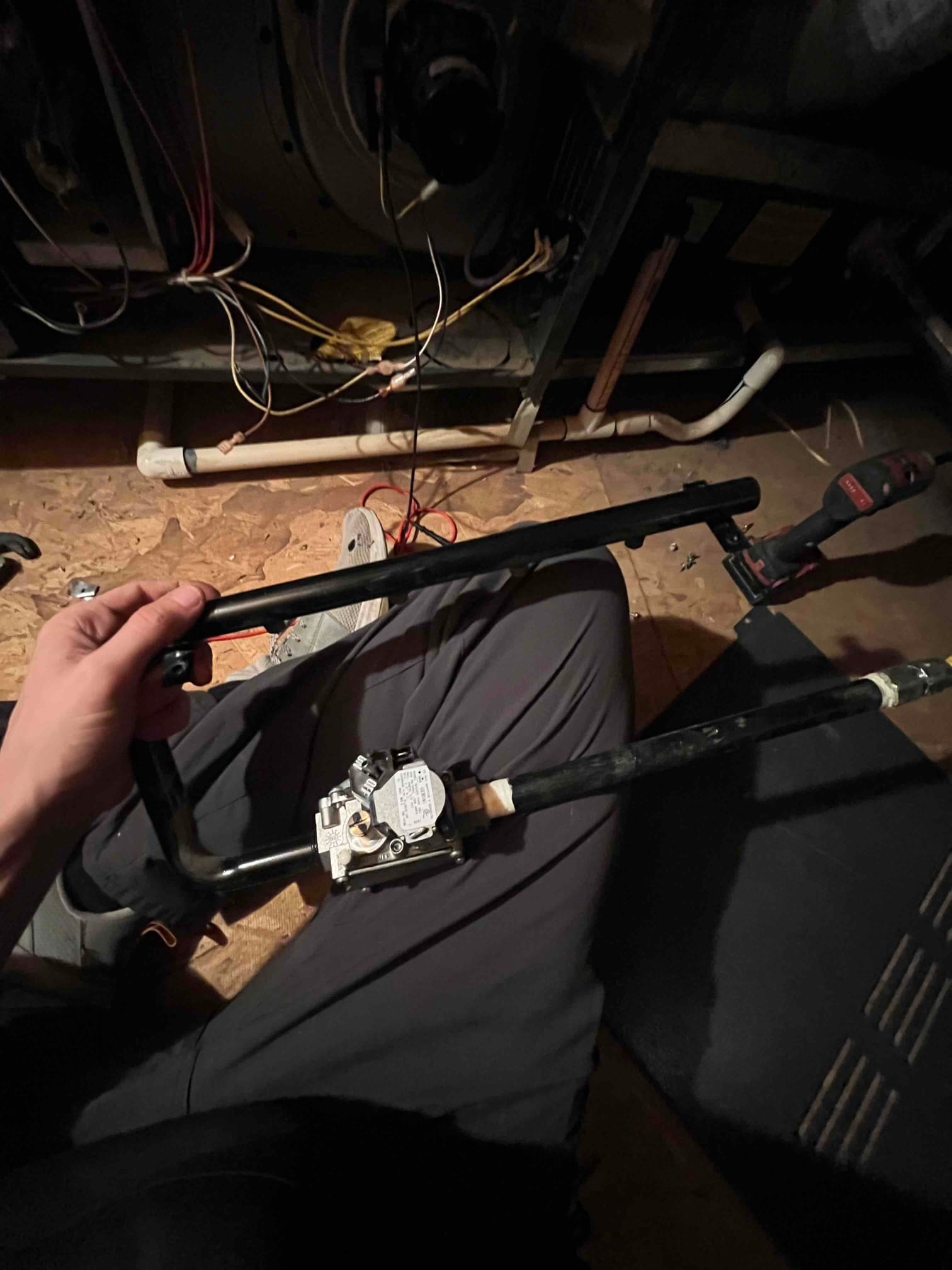Technician holds a gas valve assembly with black iron pipe in front of a furnace cabinet.
