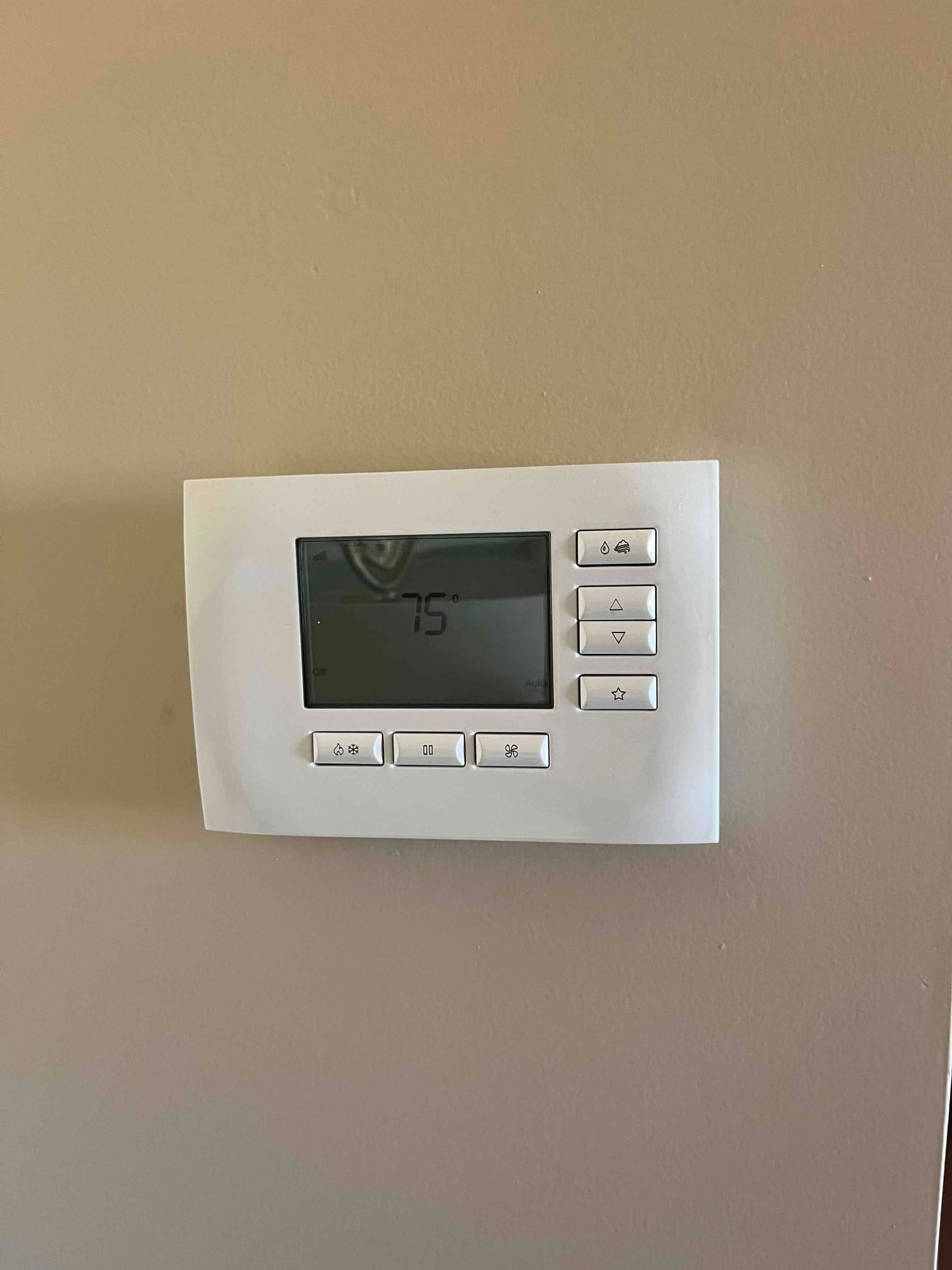 Thermostat on interior wall with backlit display reading 75° and control buttons for mode and fan.