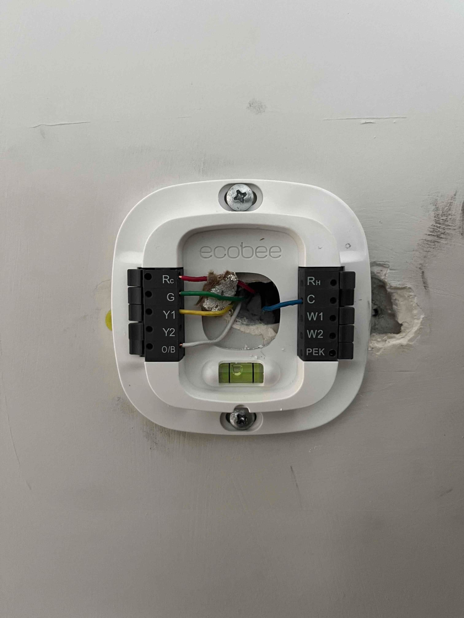 Thermostat mounting plate on wall, showing Rc, G, Y1, and C wires connected, with built-in level.