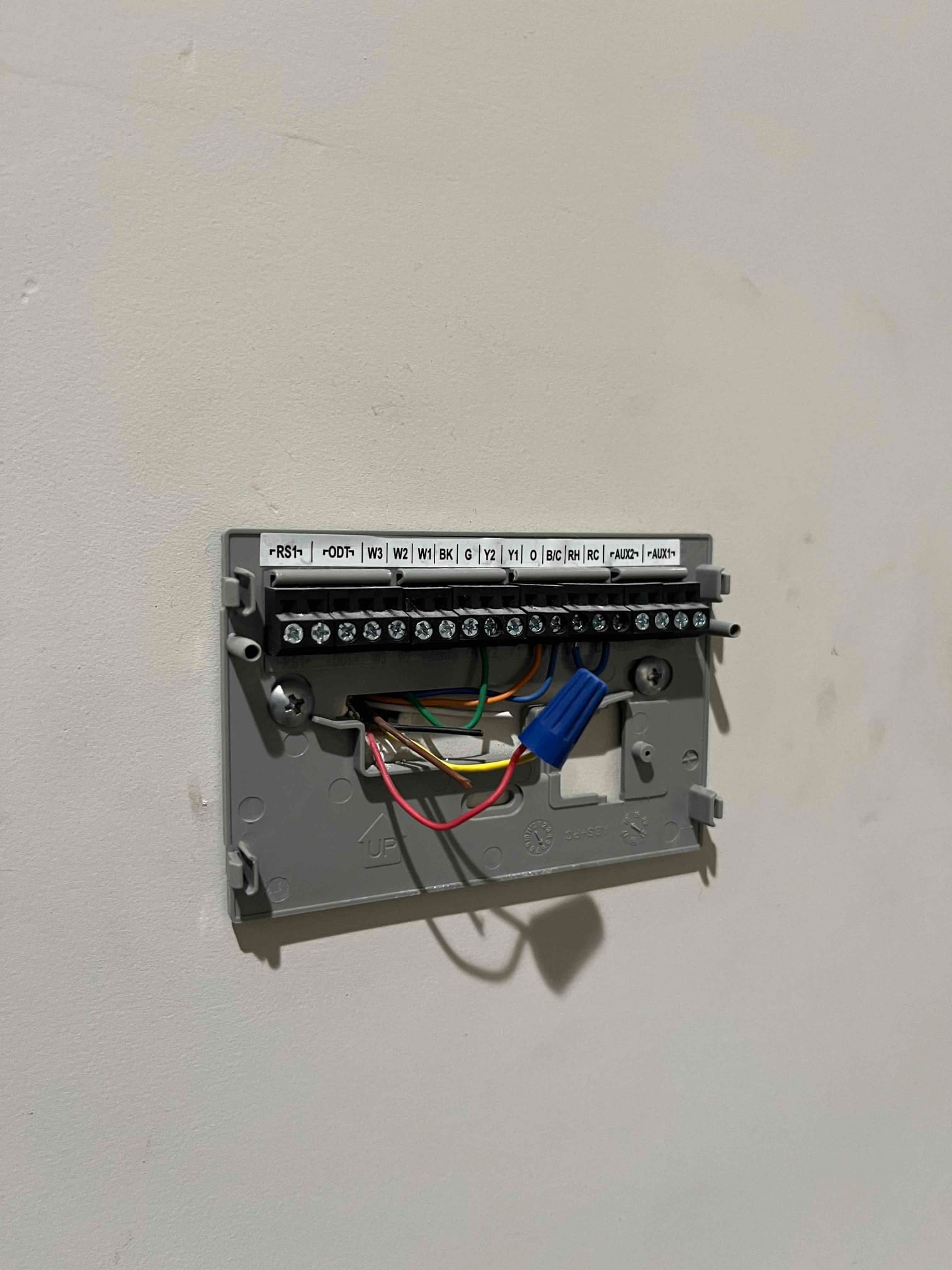 Thermostat sub-base on wall shows labeled terminals with connected red, green, yellow, white, and blue control wires.