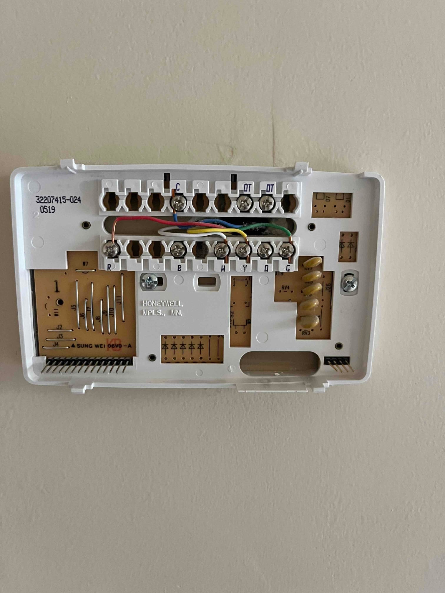 Thermostat wall plate with low-voltage wires connected to labeled terminals including R, C, W, Y, and G.