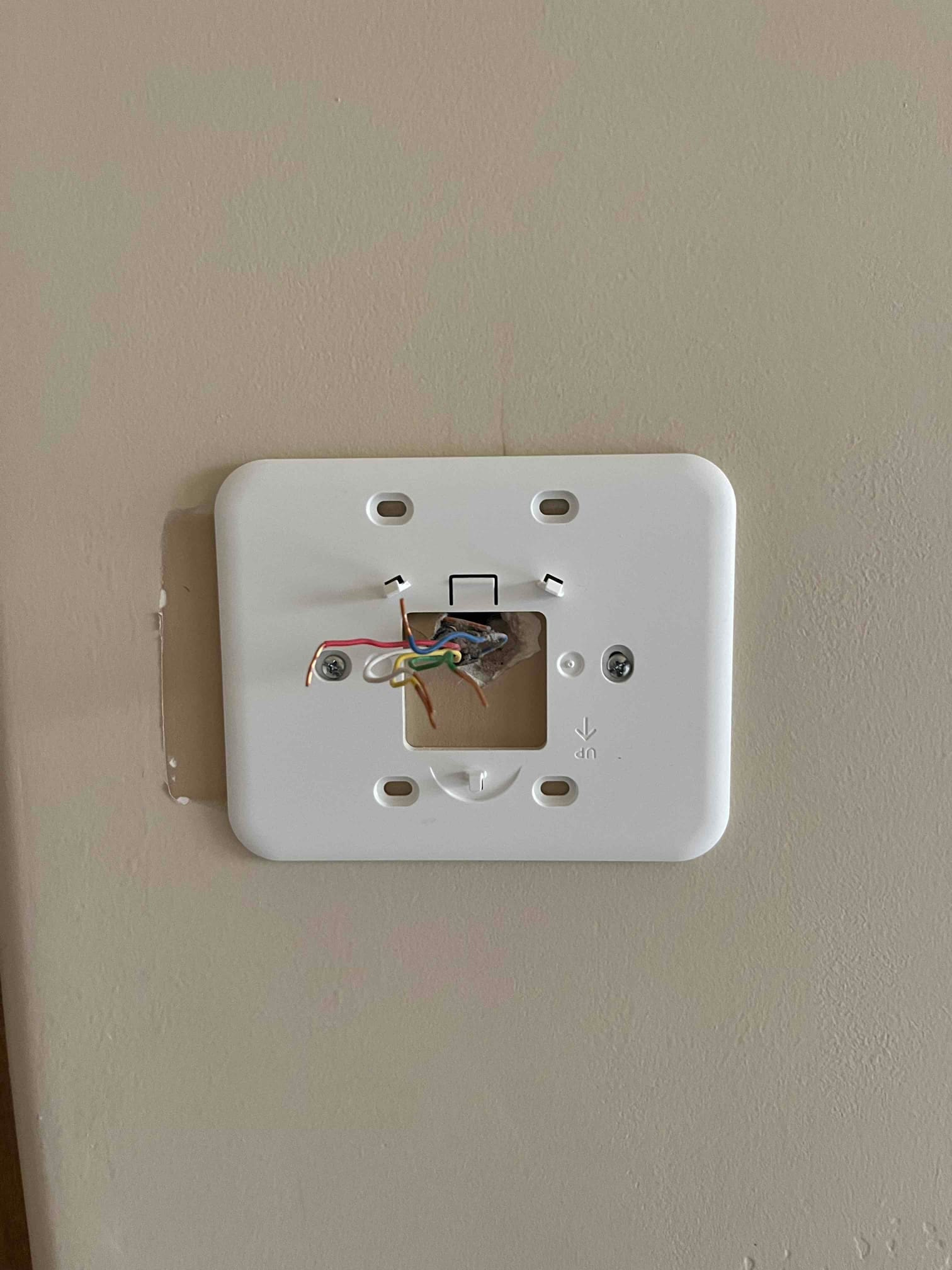 Thermostat wall plate is mounted on the wall, with low‑voltage control wires visible through the center opening.