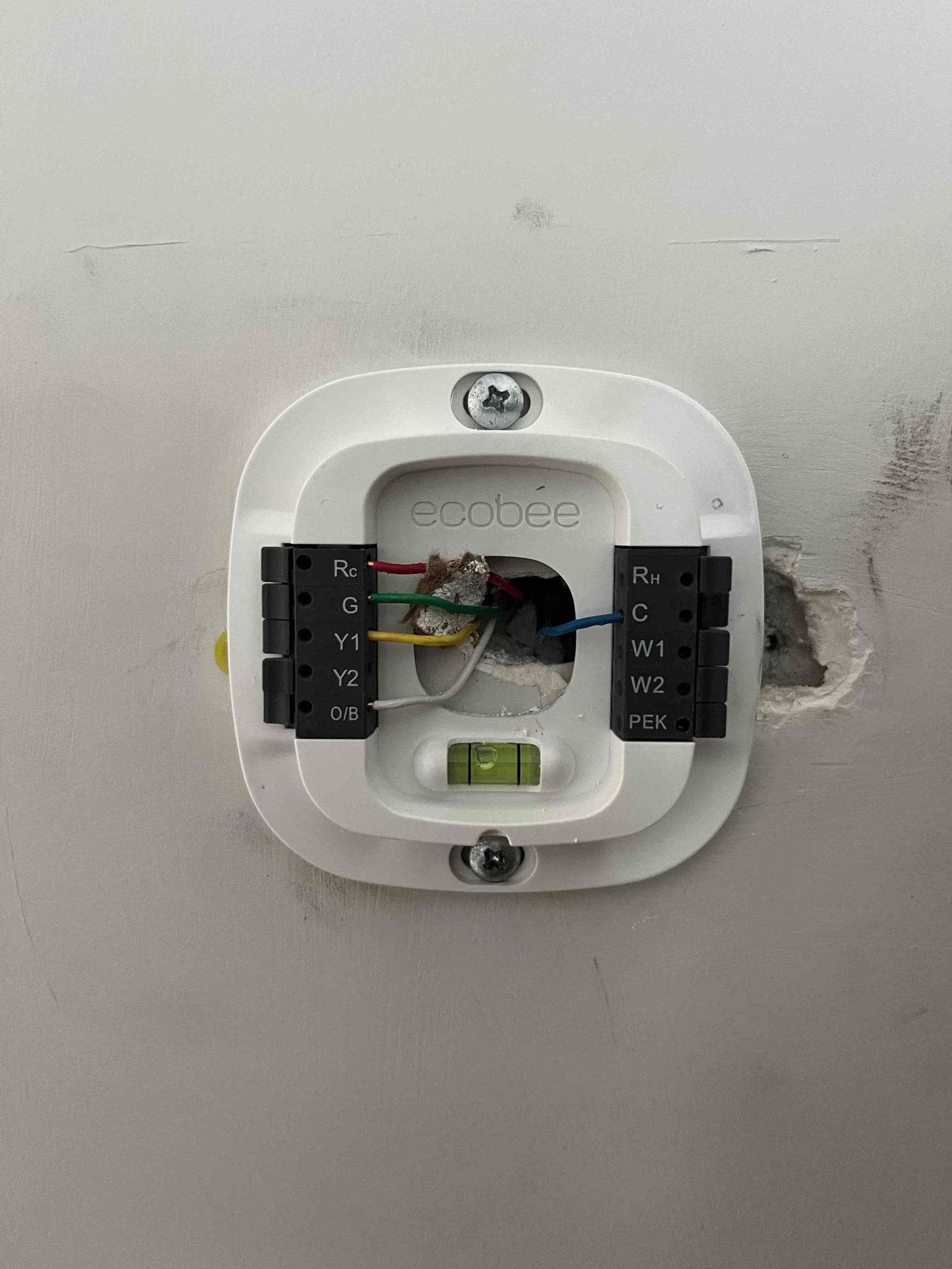 Thermostat wall plate mounted with wiring connected to Rc, G, Y1, W1, and C terminals, bubble level centered.