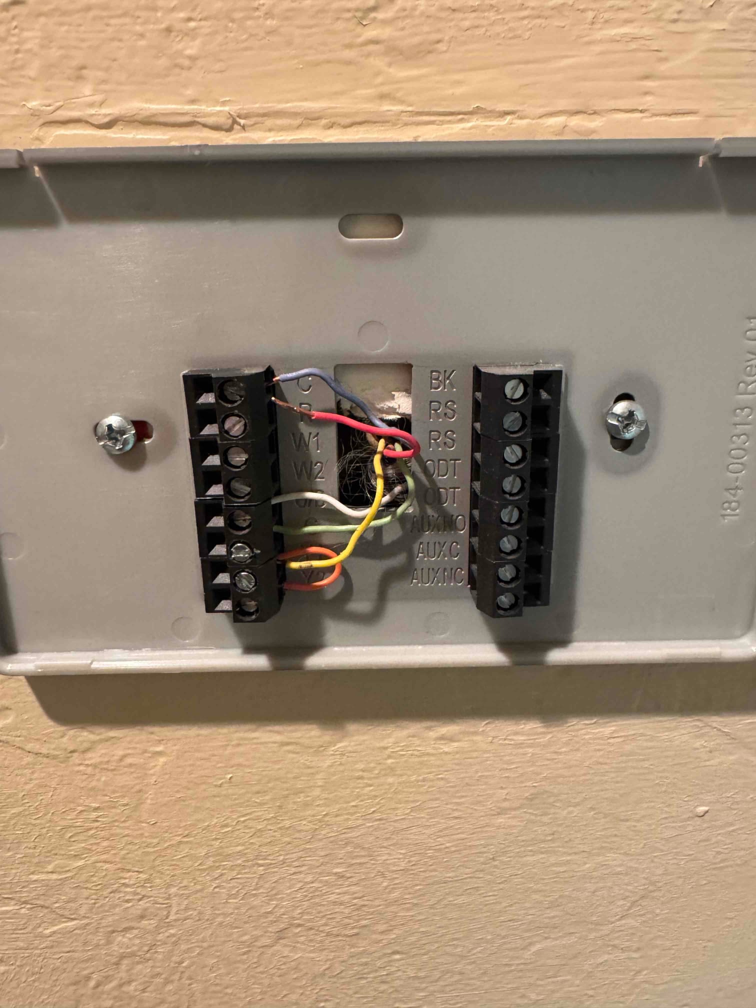 Thermostat wall plate with multiple low-voltage control wires connected to labeled terminal blocks on the backplate.