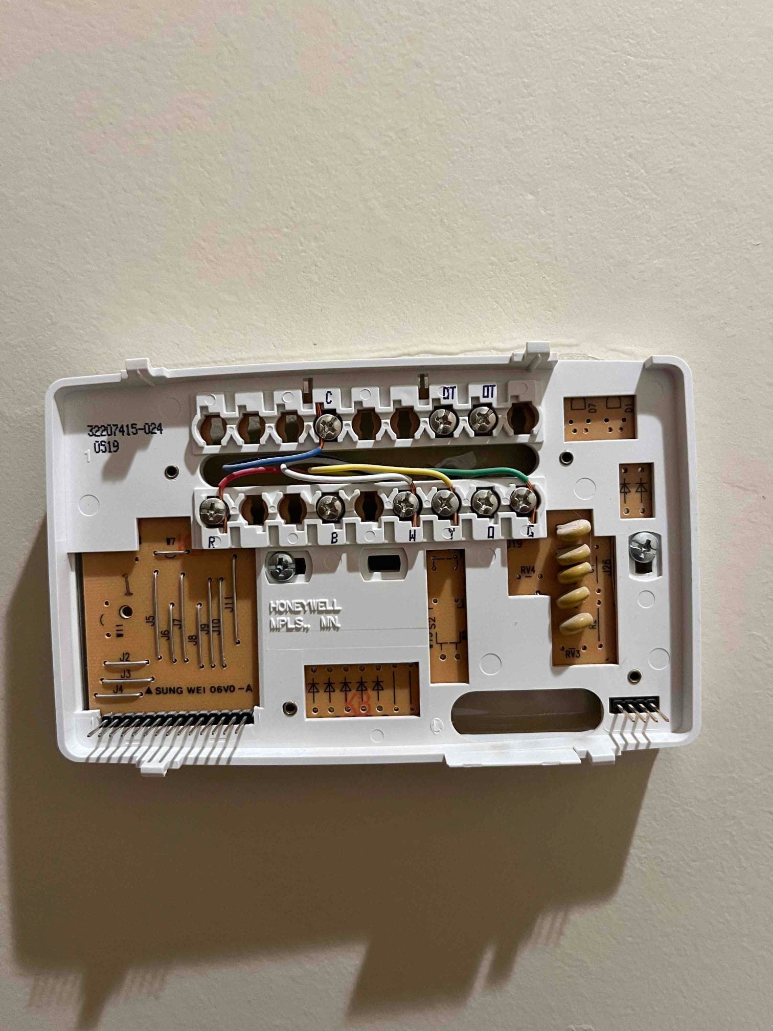 Thermostat wall plate with red, blue, yellow, green, and white low-voltage wires connected to labeled terminals.