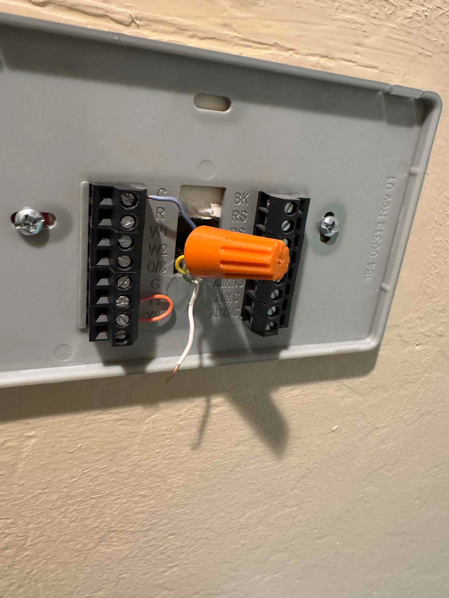 Thermostat wall plate with wiring terminals, an orange wire nut splice, and a stripped white conductor hanging loose.