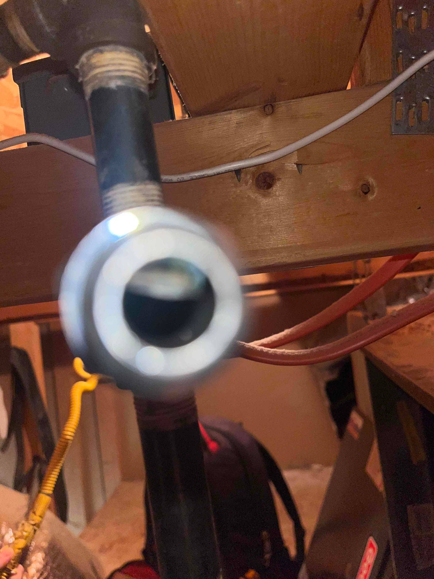 Threaded black steel pipe with elbow and open fitting in a utility area, with furnace cabinet visible nearby.