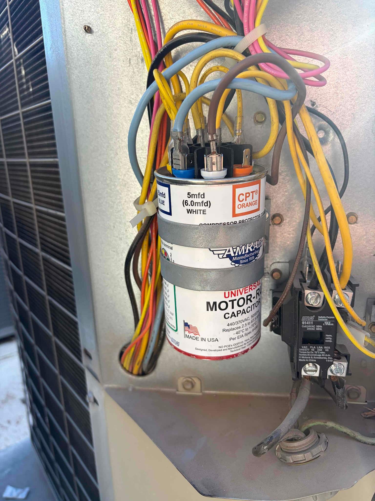 Universal motor-run capacitor with multiple wires connected, labeled 440/370 VAC, alongside contactor and control wiring inside outdoor condenser panel.