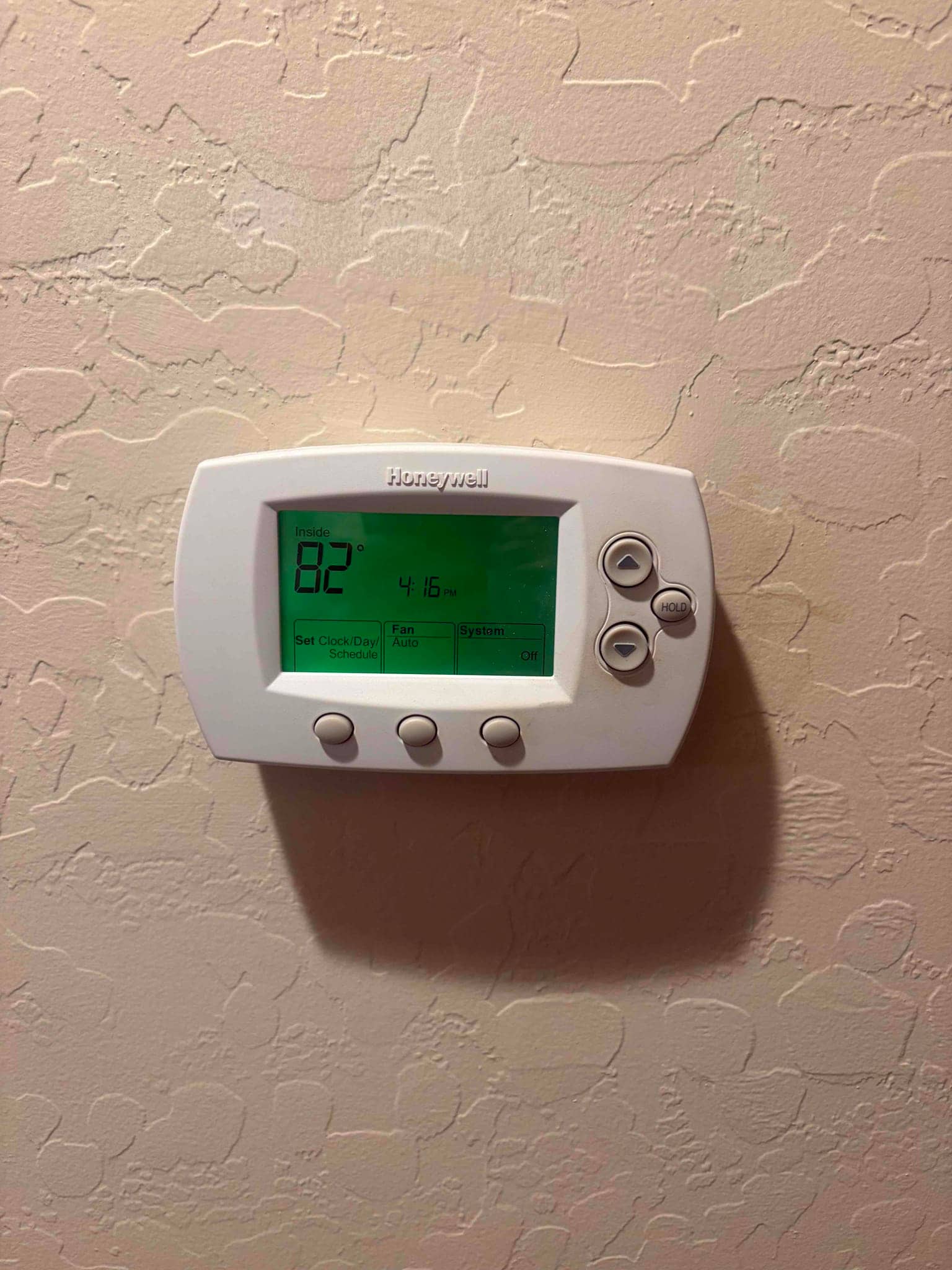 Wall-mounted digital thermostat with backlit display showing inside 82°F, time, fan set to Auto, system Off.