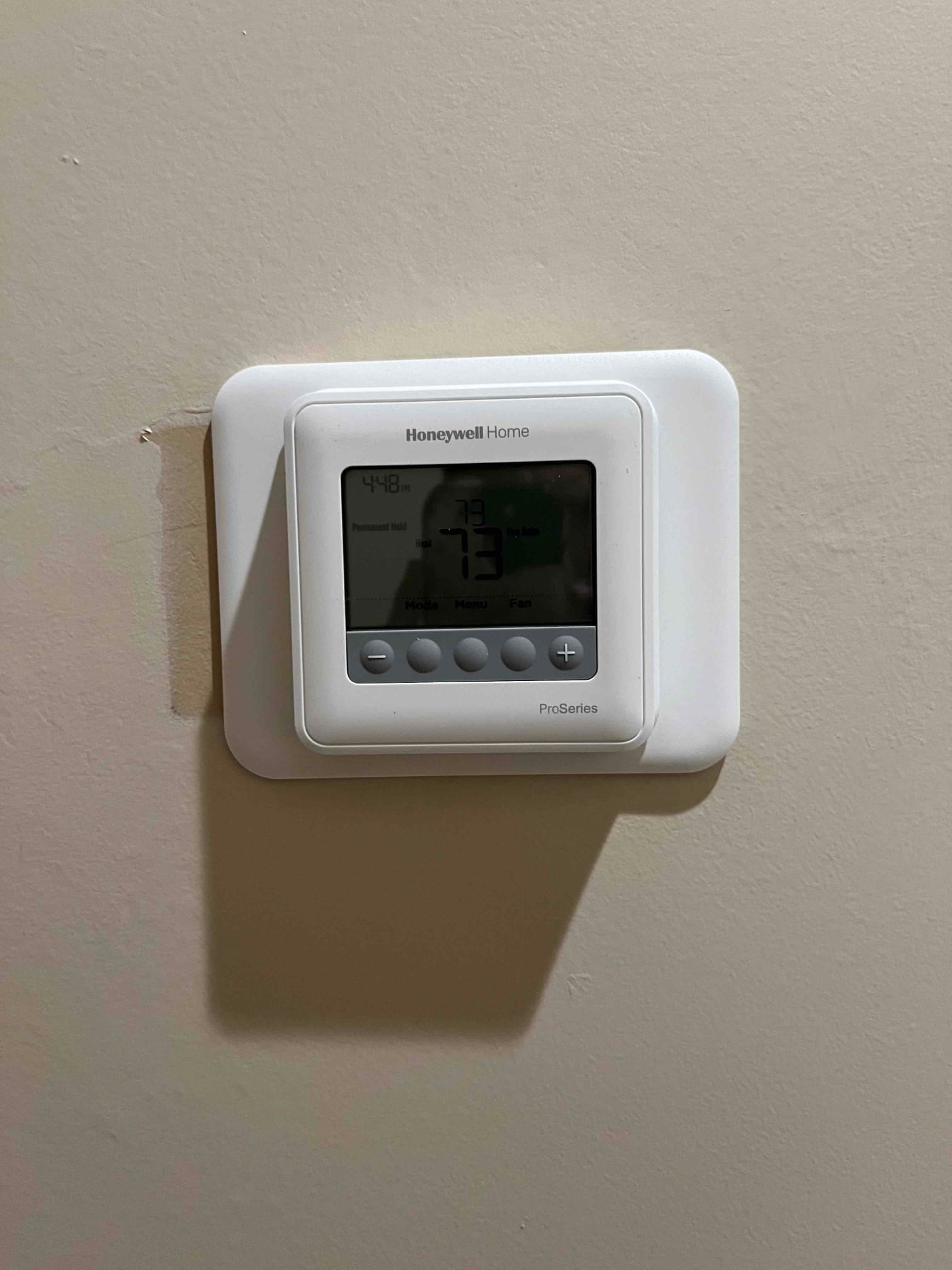 Wall-mounted digital thermostat display showing 73 on the screen with time indicator and control buttons below.