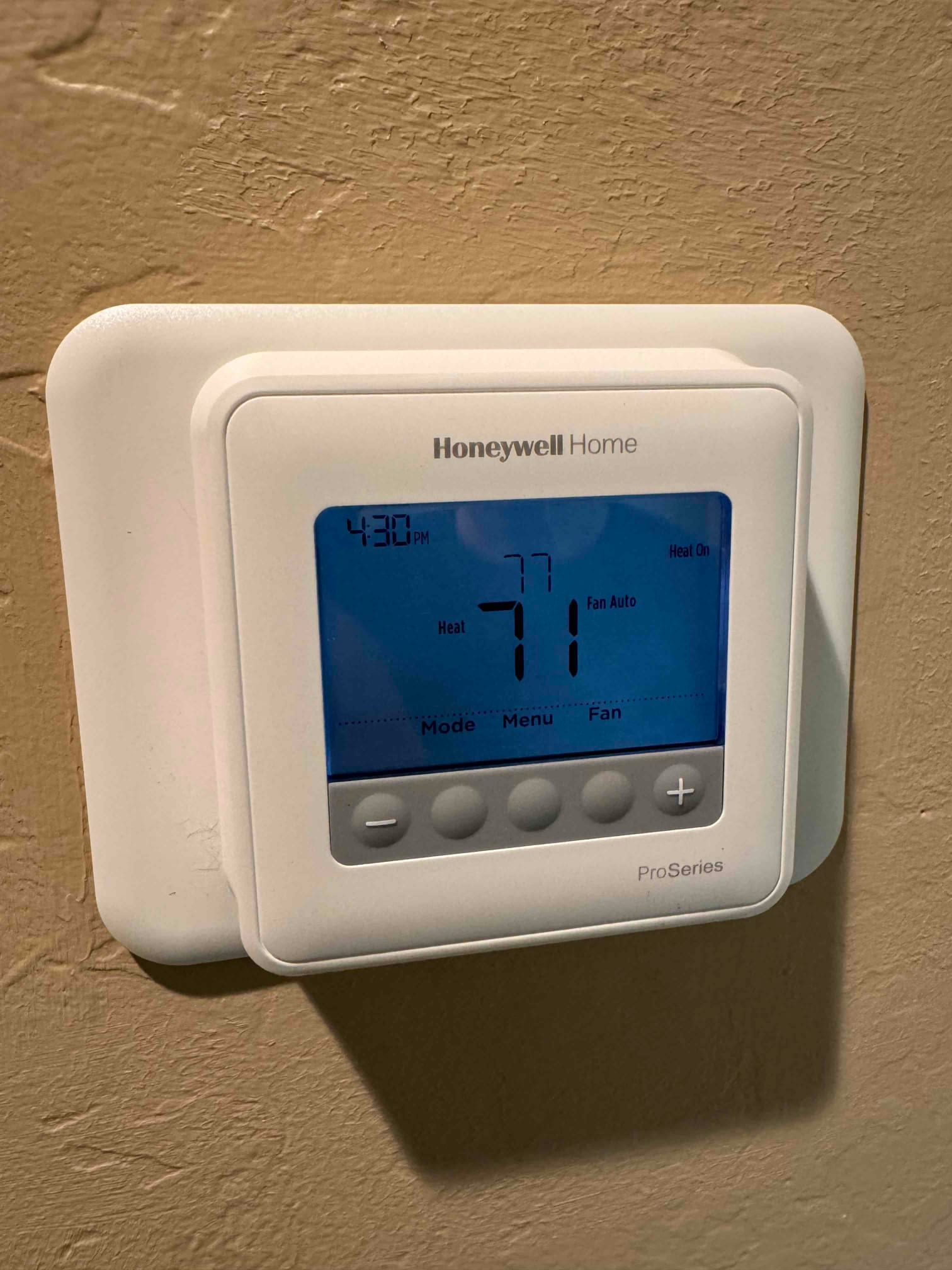 Wall-mounted digital thermostat display shows Heat mode, Fan Auto, and temperatures 71 and 77.