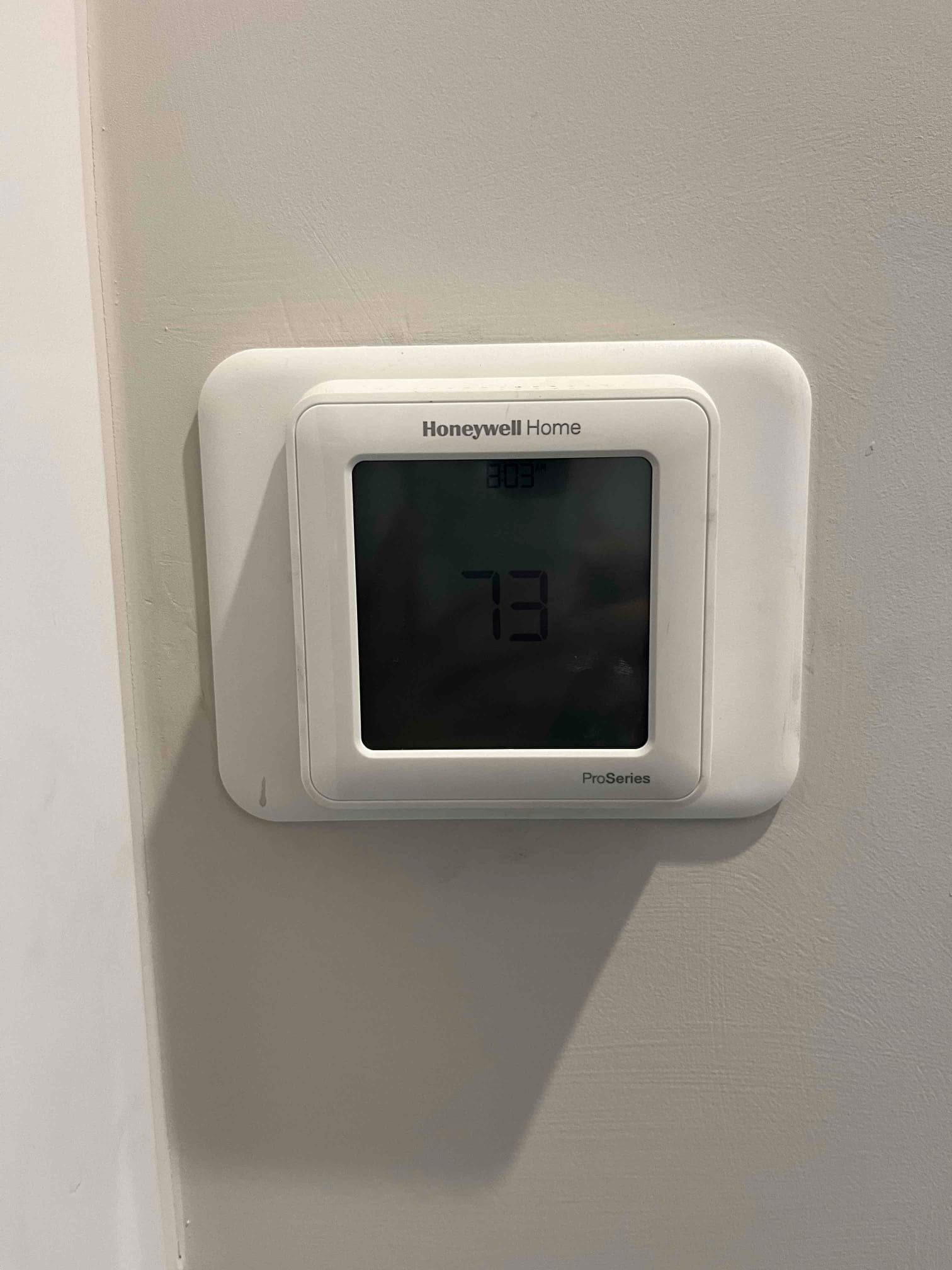 Wall-mounted digital thermostat displays 73 on its screen with the current time shown above.
