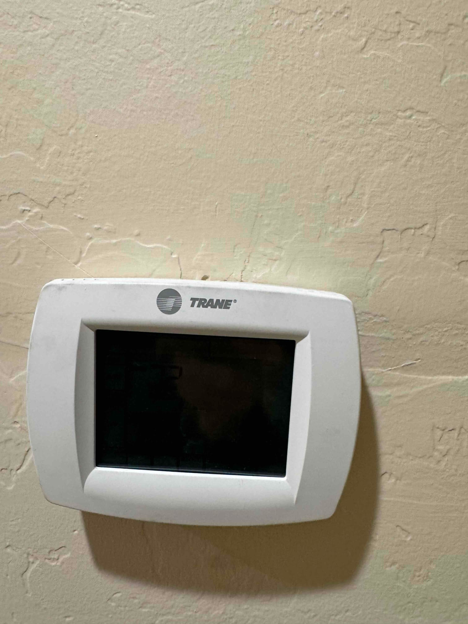 Wall-mounted programmable thermostat with a dark display screen and surrounding textured wall finish.