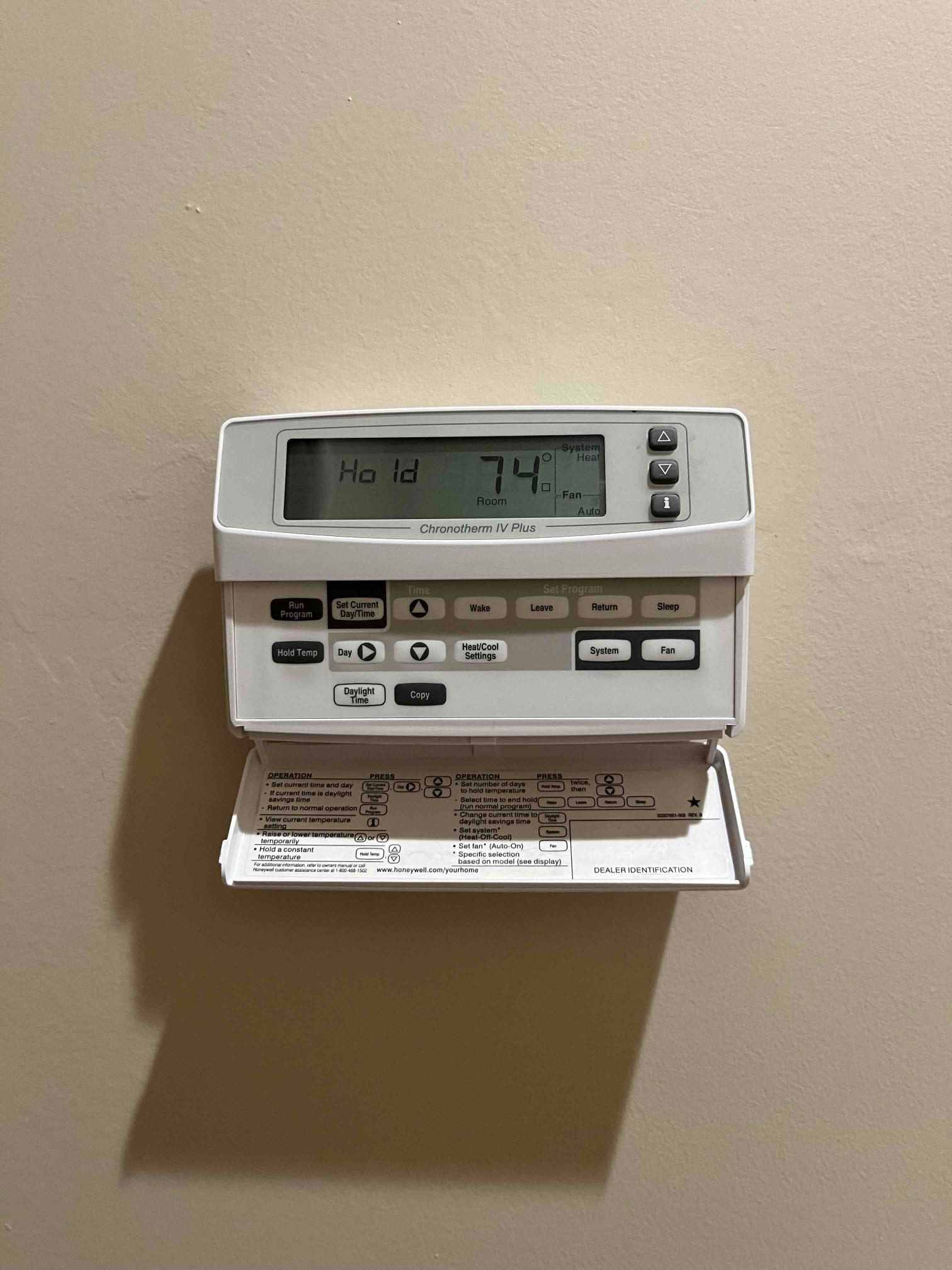 Wall-mounted programmable thermostat with display showing Hold mode and room temperature at 74°F.