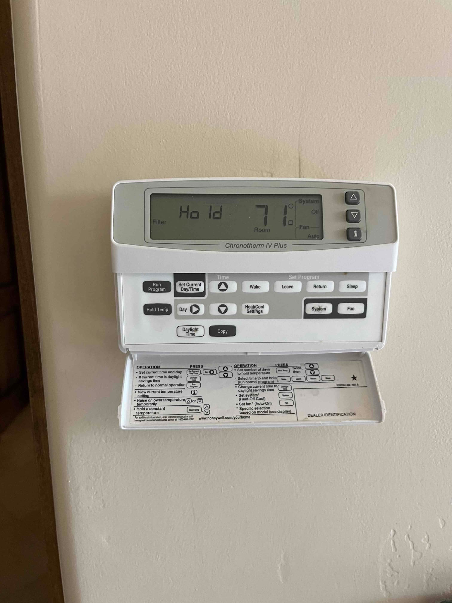 Wall-mounted programmable thermostat with drop-down cover open, display shows Hold mode and 71 degrees.