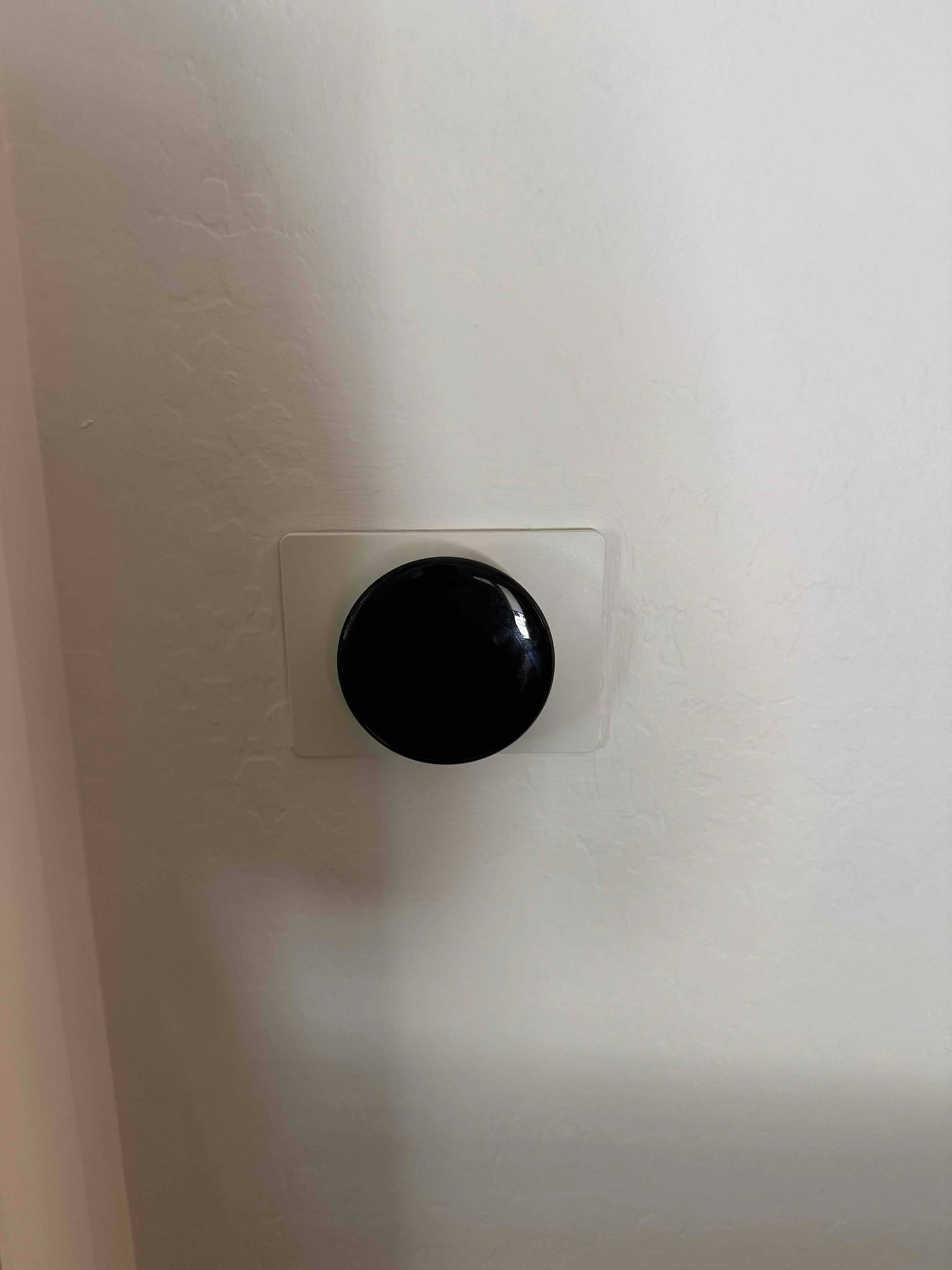 Wall-mounted round thermostat with a dark, inactive screen, centered on a textured interior wall.
