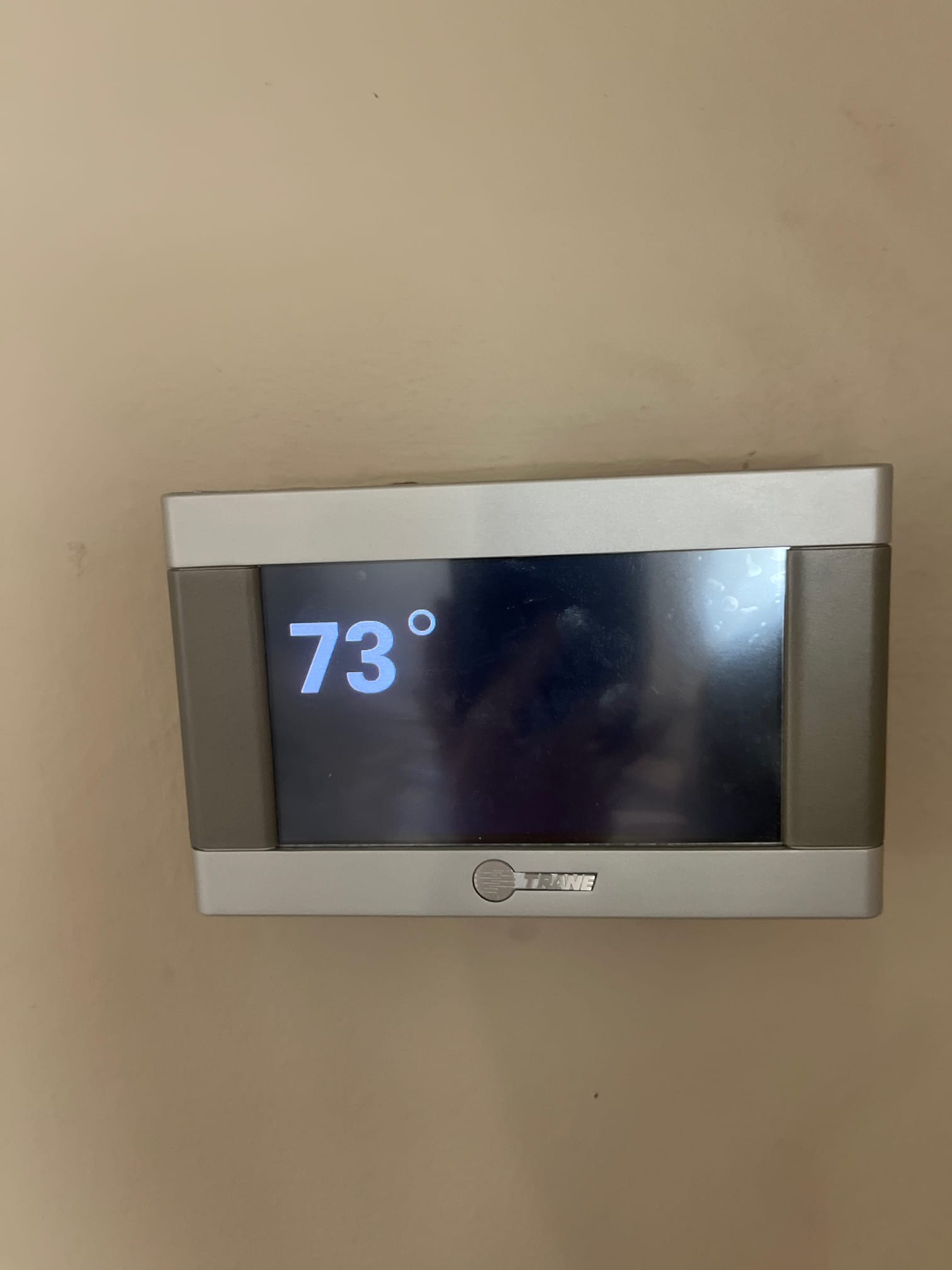 Wall-mounted thermostat display shows 73° on the screen, with smudges visible on the glossy surface.