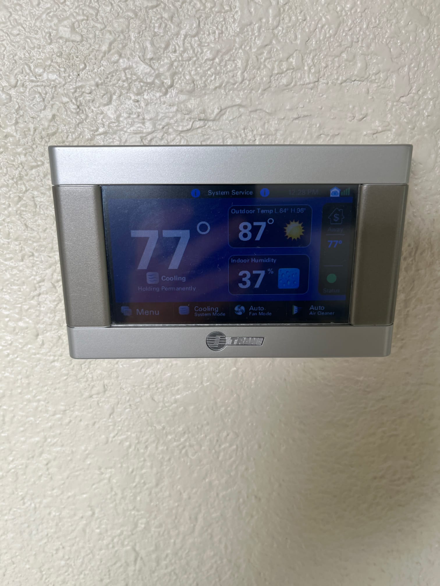 Wall-mounted touchscreen thermostat shows 77°F indoor temperature, 87°F outdoor temperature, and 37% indoor humidity during cooling mode.