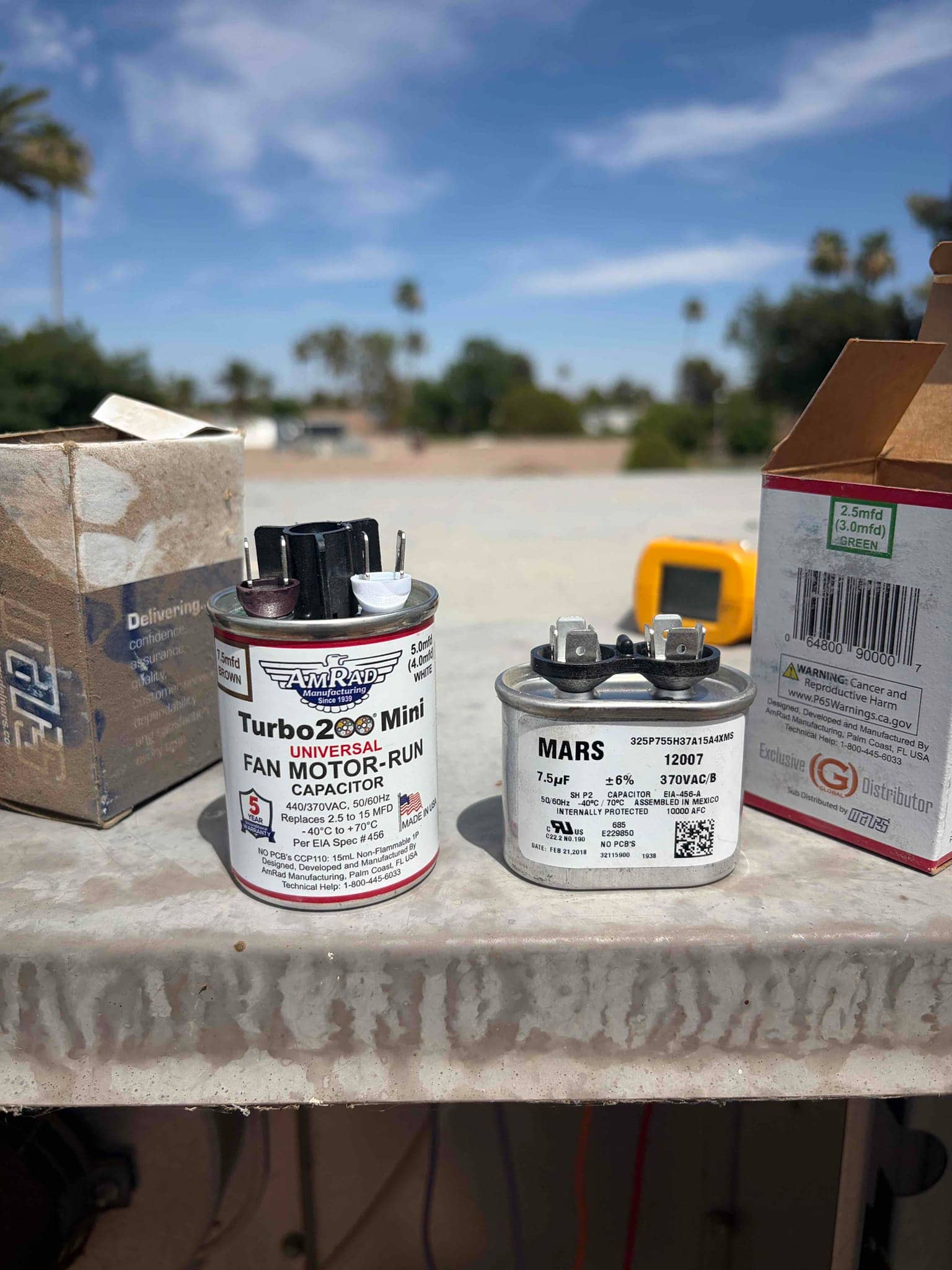 Two fan motor run capacitors on a service surface, right unit labeled 7.5 μF ±6% 370VAC, left labeled 440/370VAC.