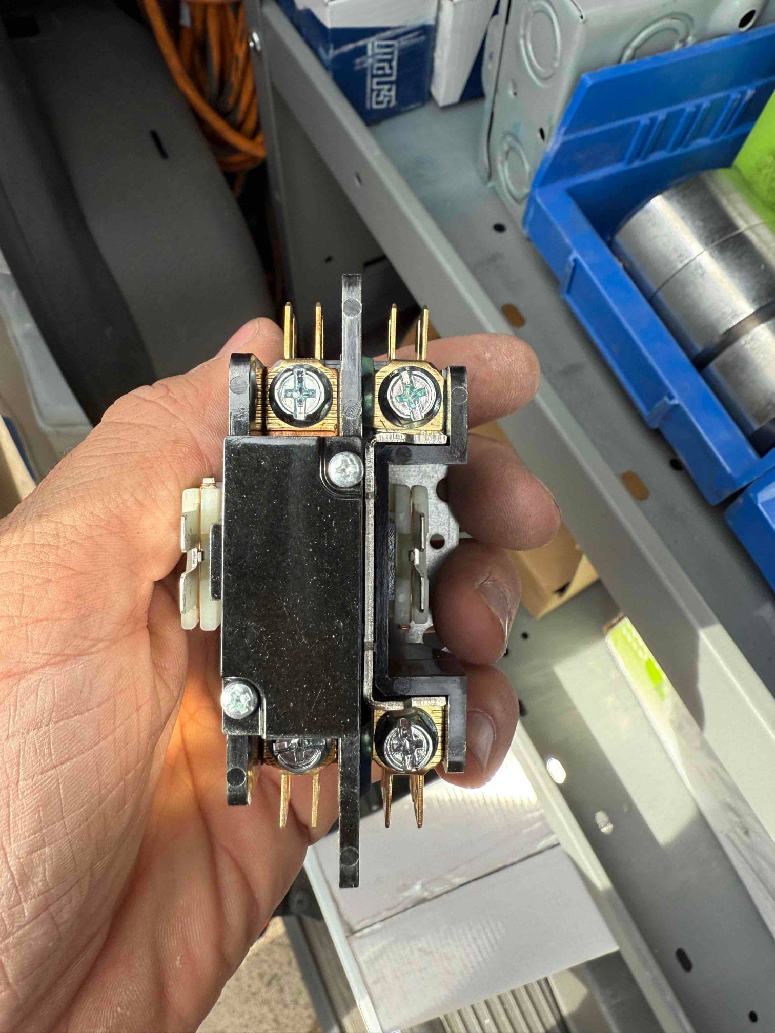 HVAC contactor held in hand, showing screw terminals and brass contact pins with mounting bracket visible.