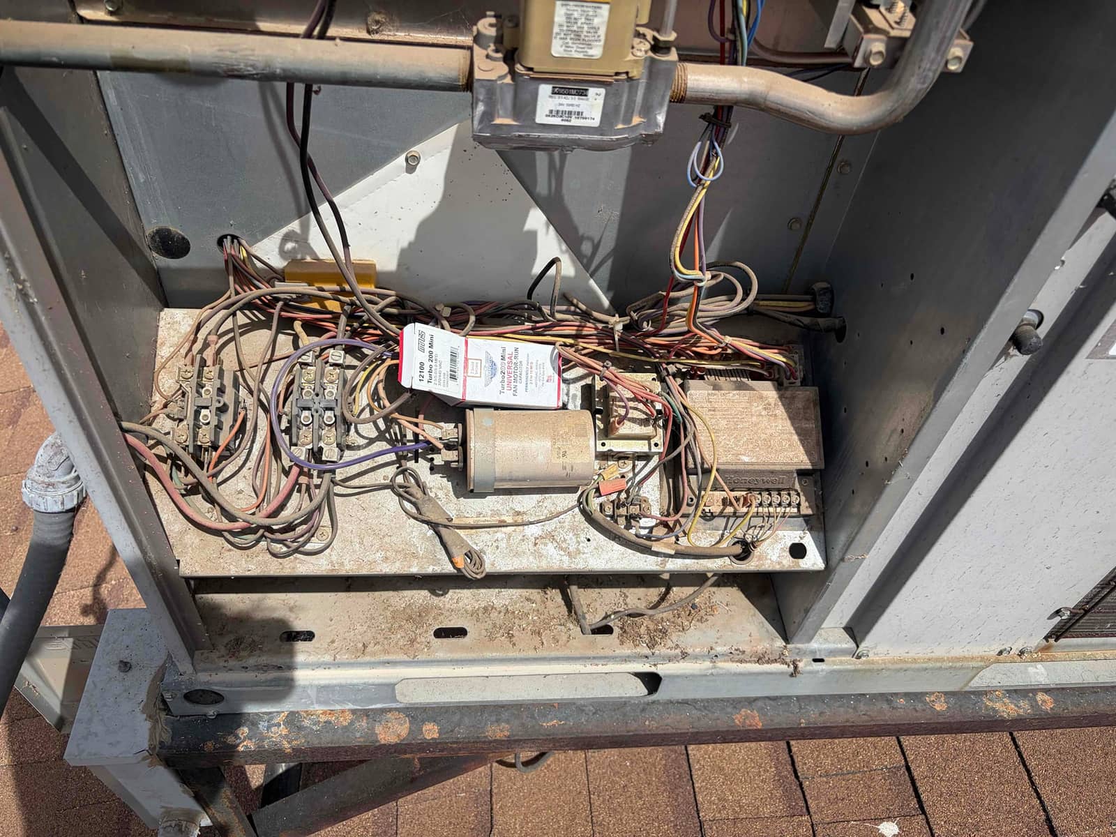 Open HVAC unit control compartment exposing wiring, terminal blocks, a metal run capacitor, and dusty control components on the mounting panel.