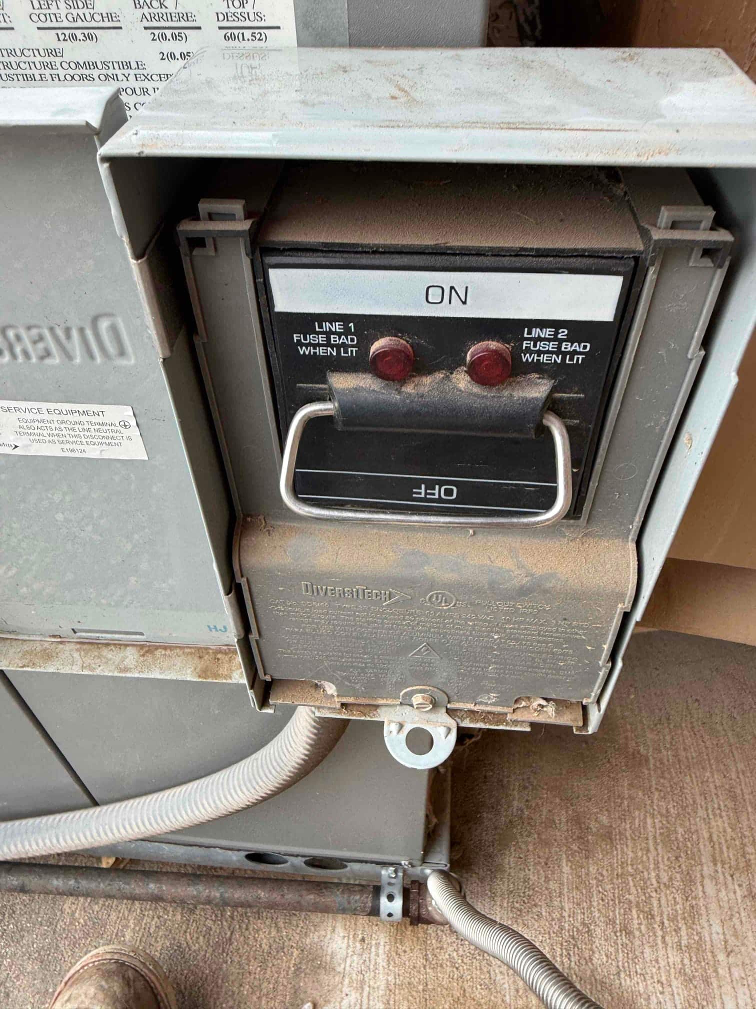 Outdoor air conditioner disconnect shows pull handle in the ON position with indicator lenses for line fuses and flexible metallic conduits attached.