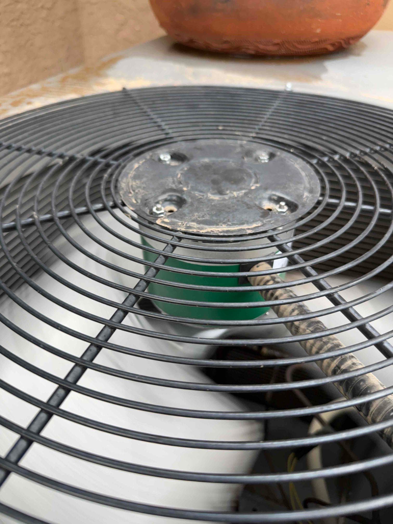Outdoor condenser fan grille and hub with dust and screws visible, fan motor housing and wiring below.