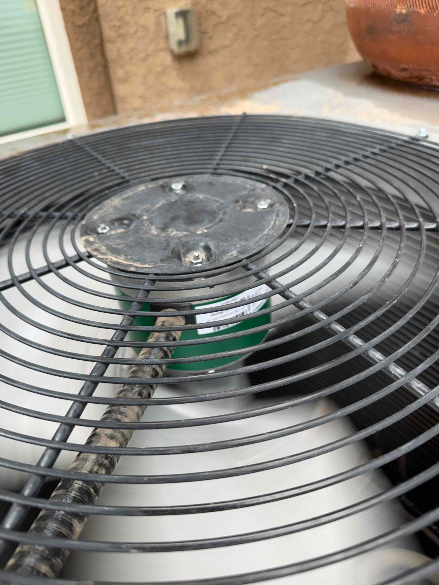 Outdoor condenser fan guard and motor hub visible, with a green cylindrical component mounted below the grille.