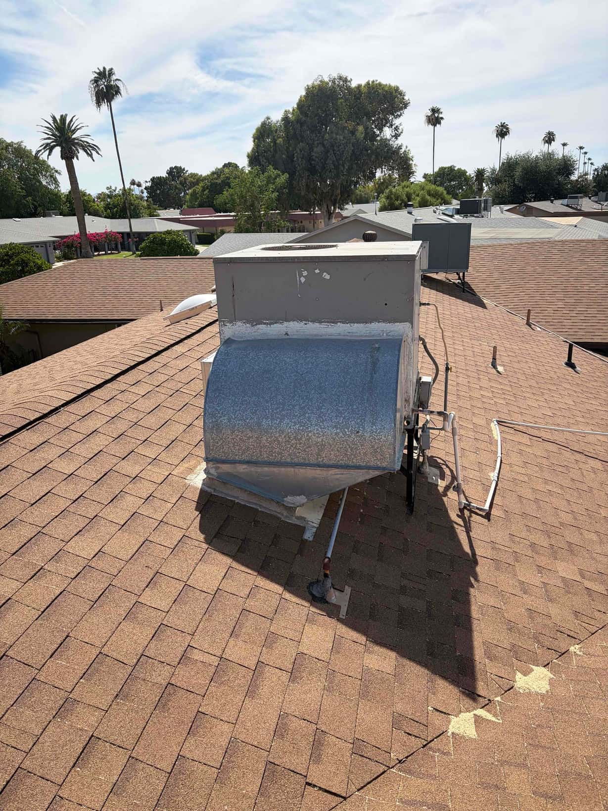 Rooftop HVAC unit with galvanized discharge duct and electrical conduit on asphalt-shingle roof, photographed during a residential service visit.
