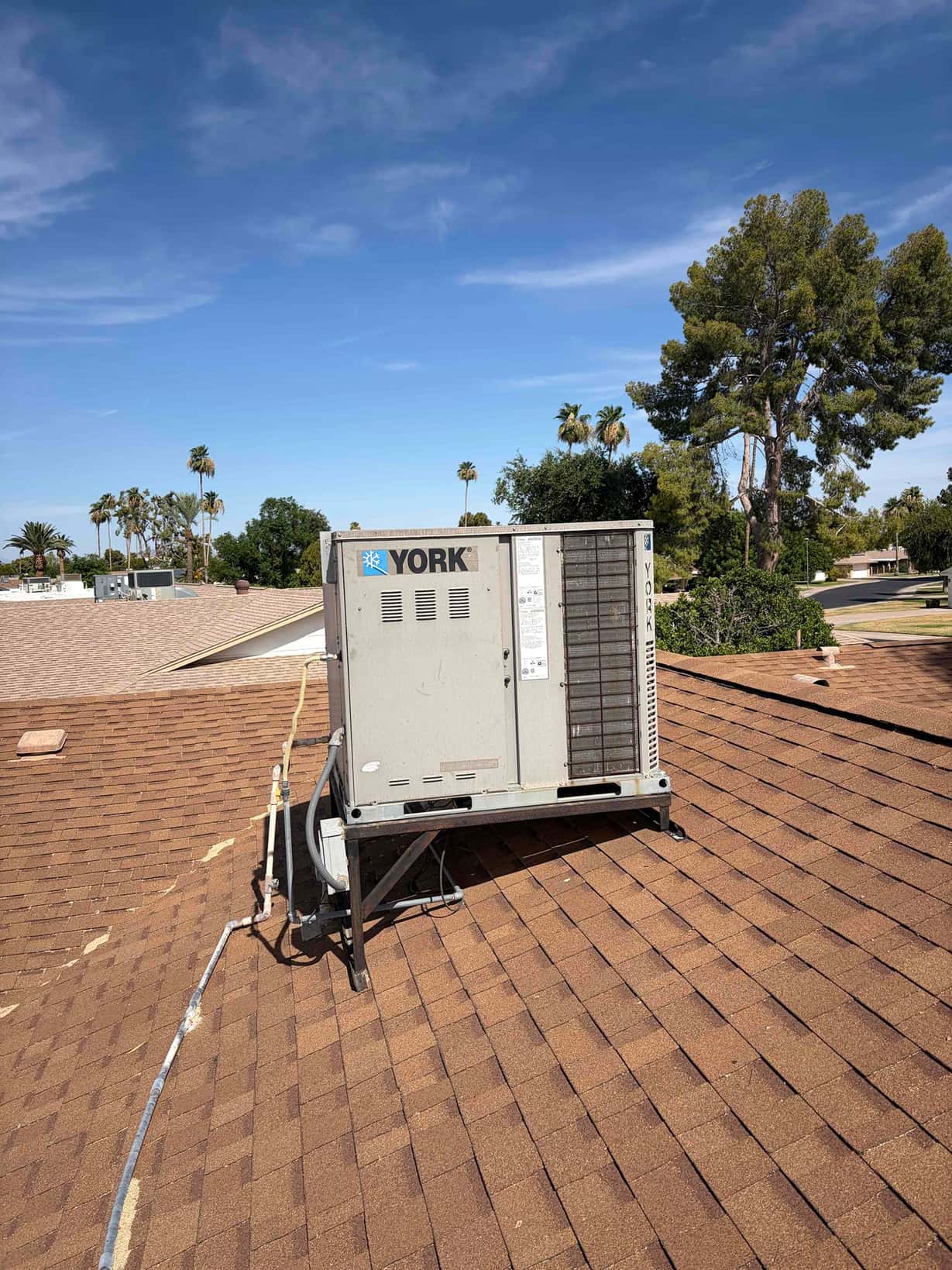 Rooftop packaged HVAC unit on a metal stand with connected refrigerant and electrical conduits.