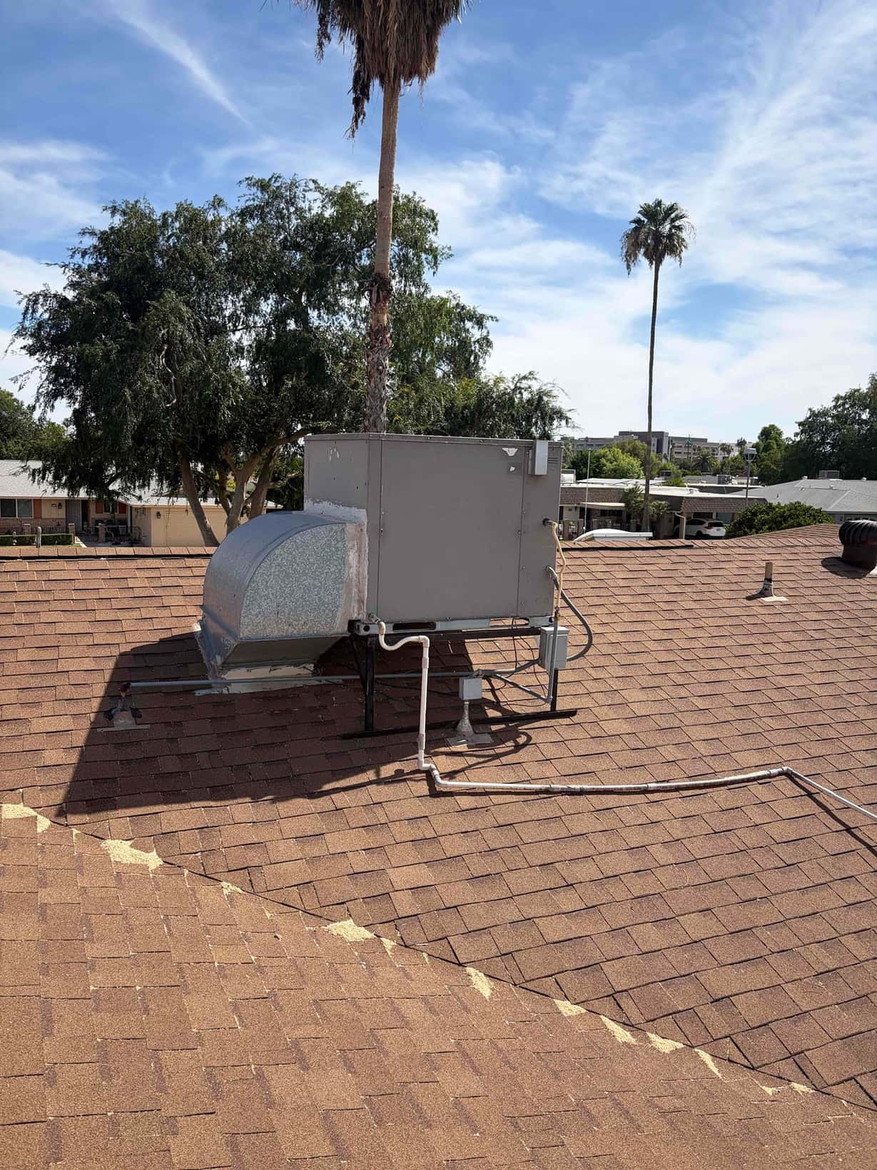 Rooftop packaged HVAC unit on shingle roof with metal duct transition and exterior electrical conduit and piping.