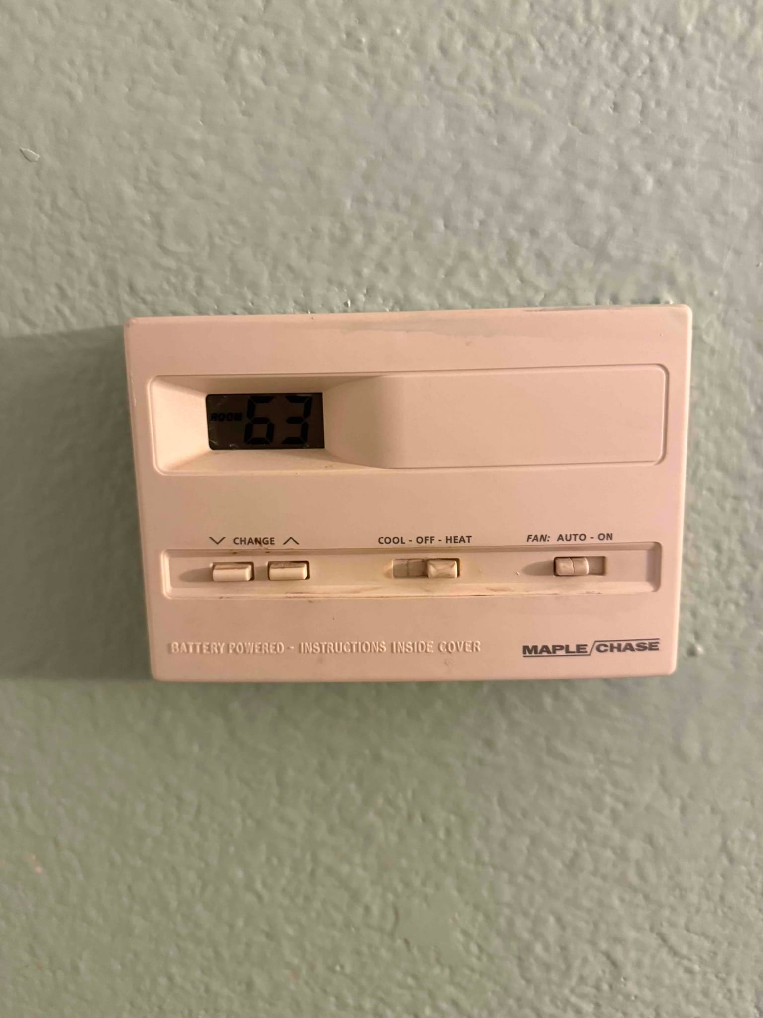 Wall-mounted digital thermostat shows room temperature at 63 with slide switches for system mode, fan, and temperature adjustment.
