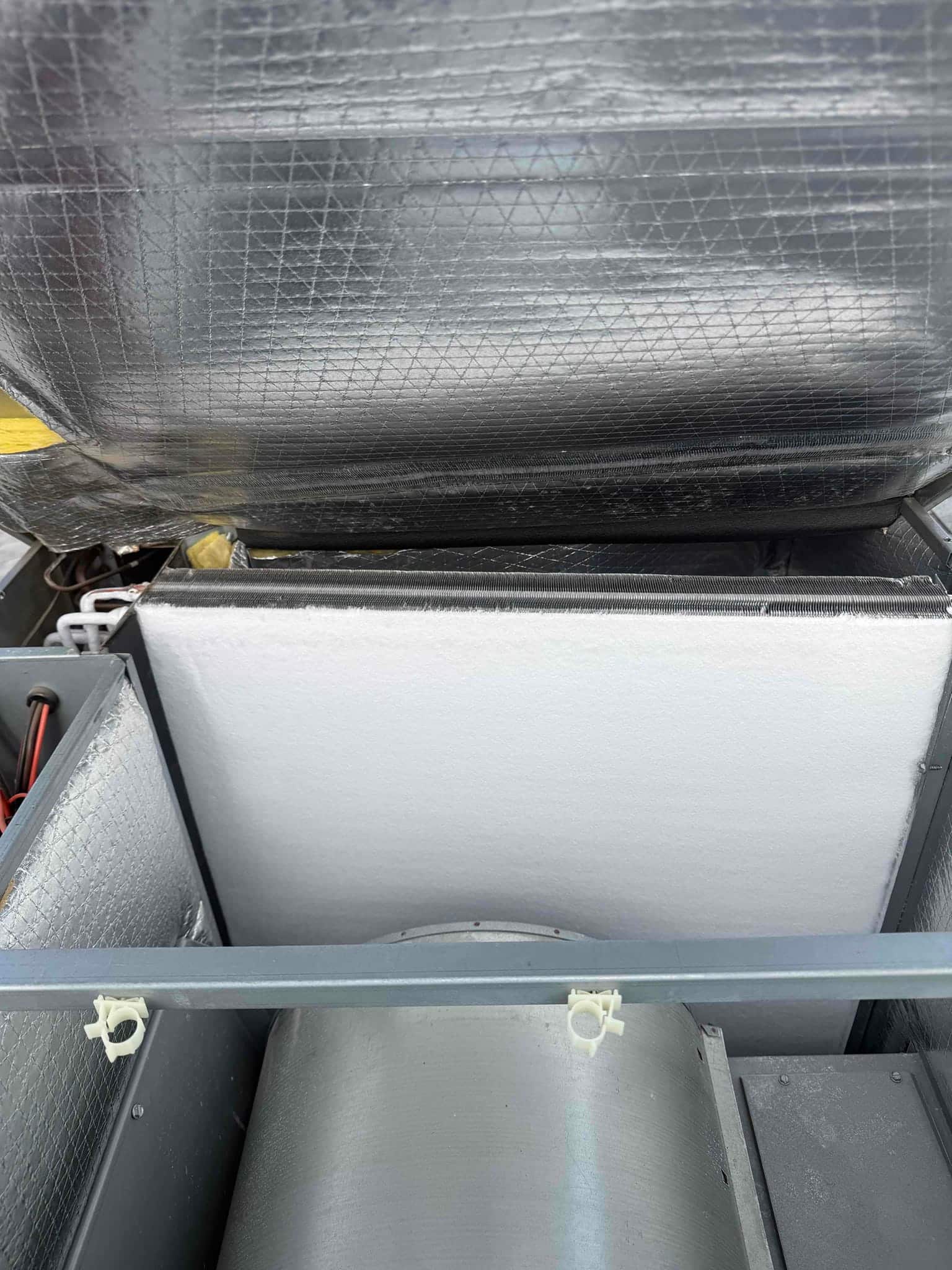 Air handler interior showing cylindrical blower housing beneath a white panel and foil-faced insulation.