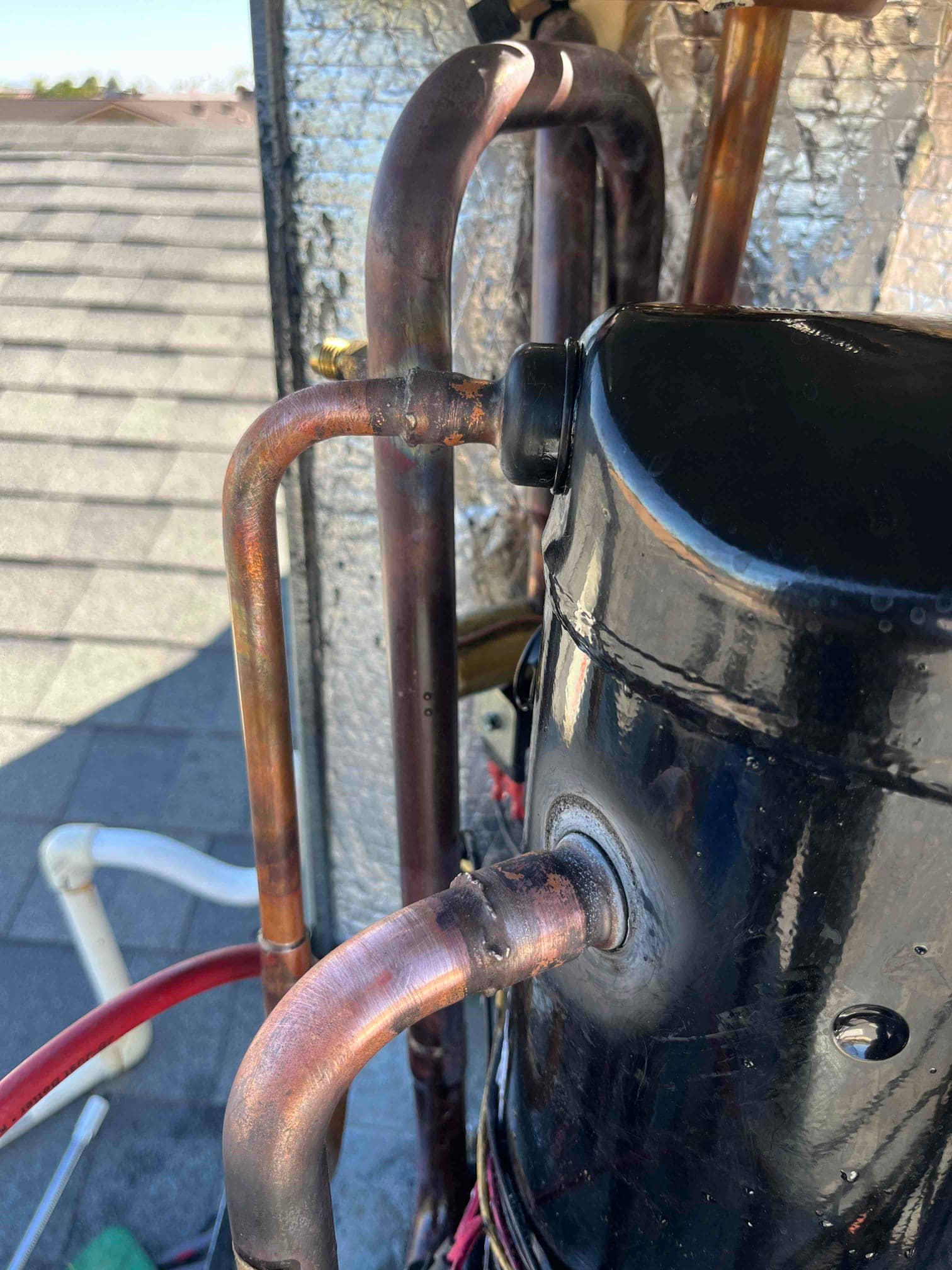 Brazed copper refrigerant lines connect to a black hermetic compressor inside the outdoor unit, showing heat marks at joints.