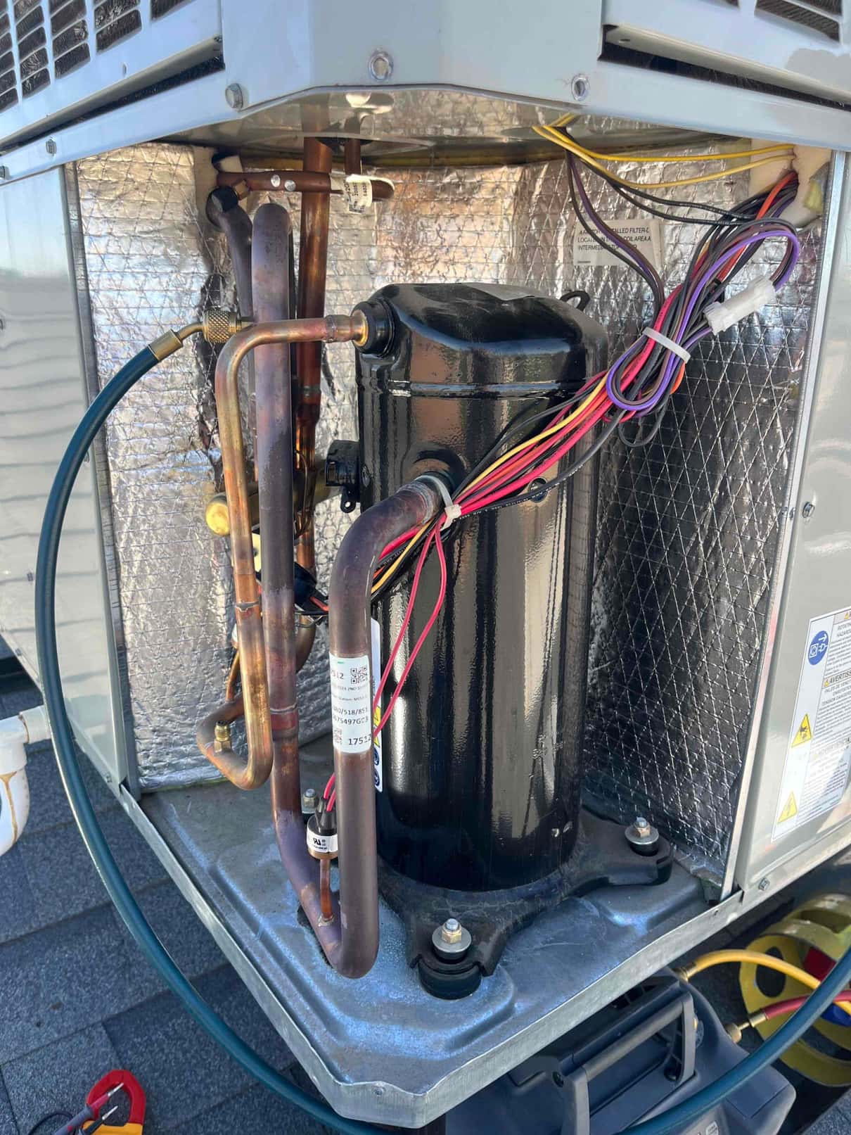 Condenser compartment open, showing black compressor, copper refrigerant lines with service hoses attached, and a bundled wiring harness.
