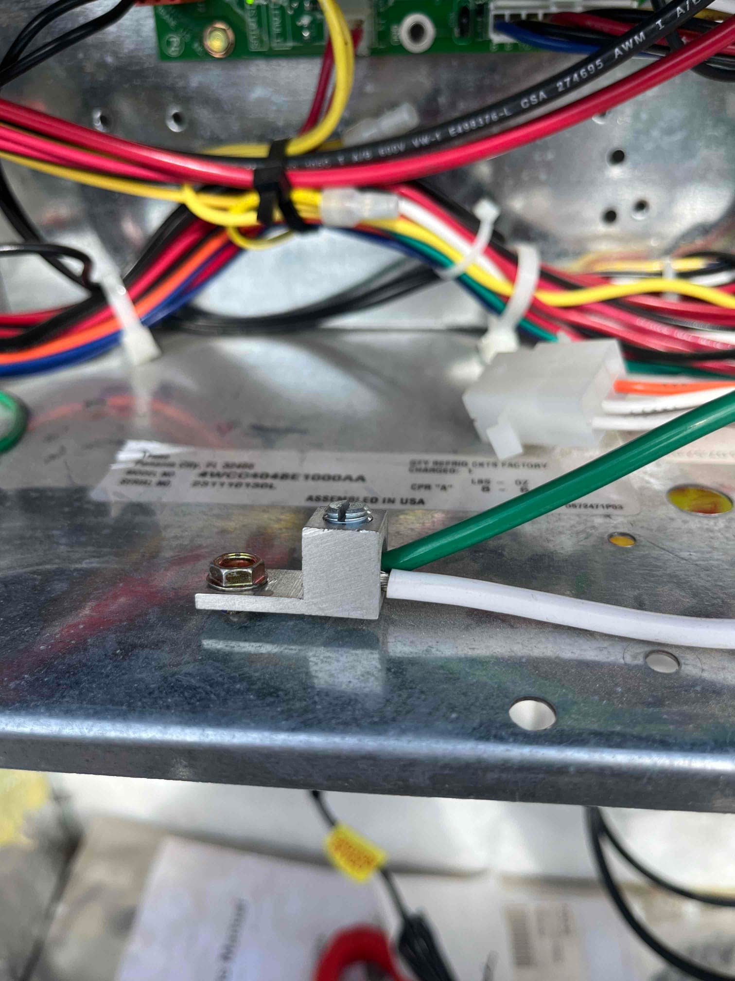 Green ground wire secured to a chassis grounding lug, with a white conductor routed alongside and multicolored control wiring above.