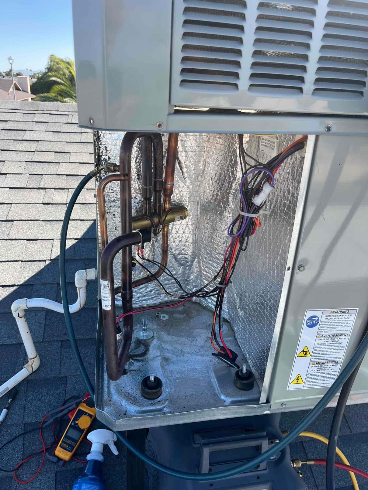 Open rooftop unit compartment showing copper refrigerant lines, wiring harness, insulated cabinet, and service hoses on the roof.
