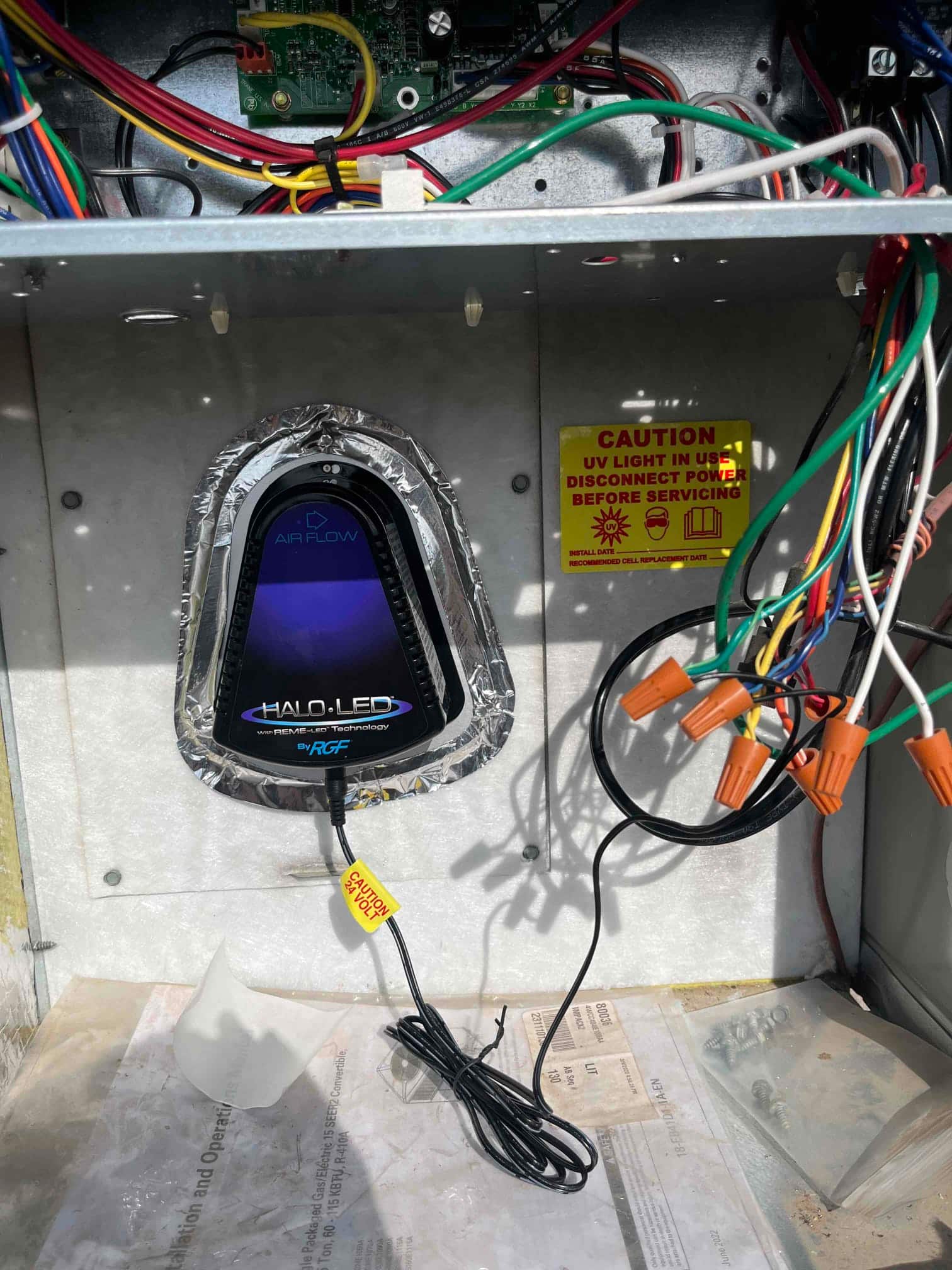 UV air purifier installed inside the air handler cabinet with wiring connections and a caution label visible.