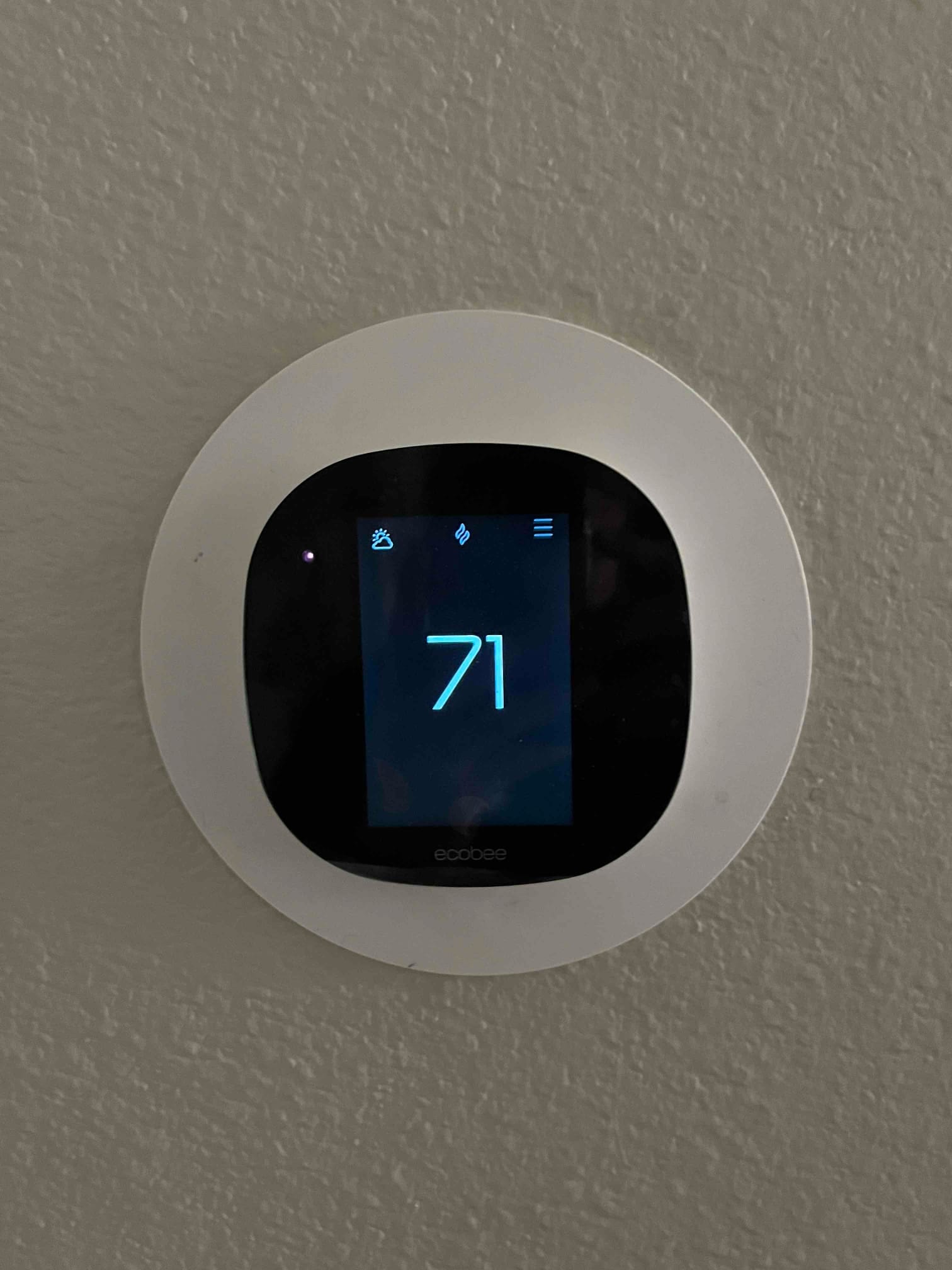 Wall-mounted smart thermostat displays 71 degrees with icons on the screen indicating system status.