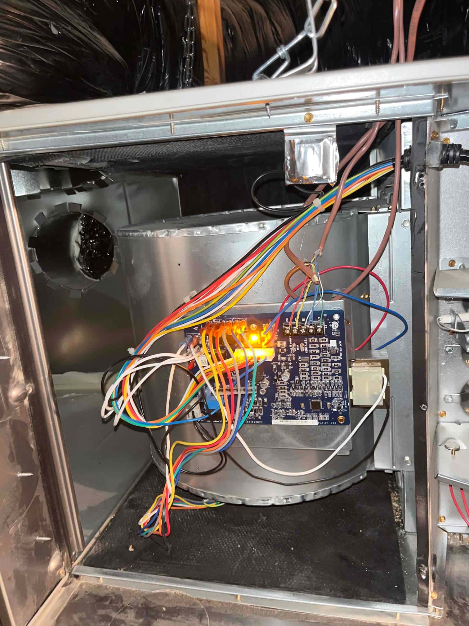 Air handler blower compartment open, showing control board with multiple connected wires and illuminated diagnostic LEDs.