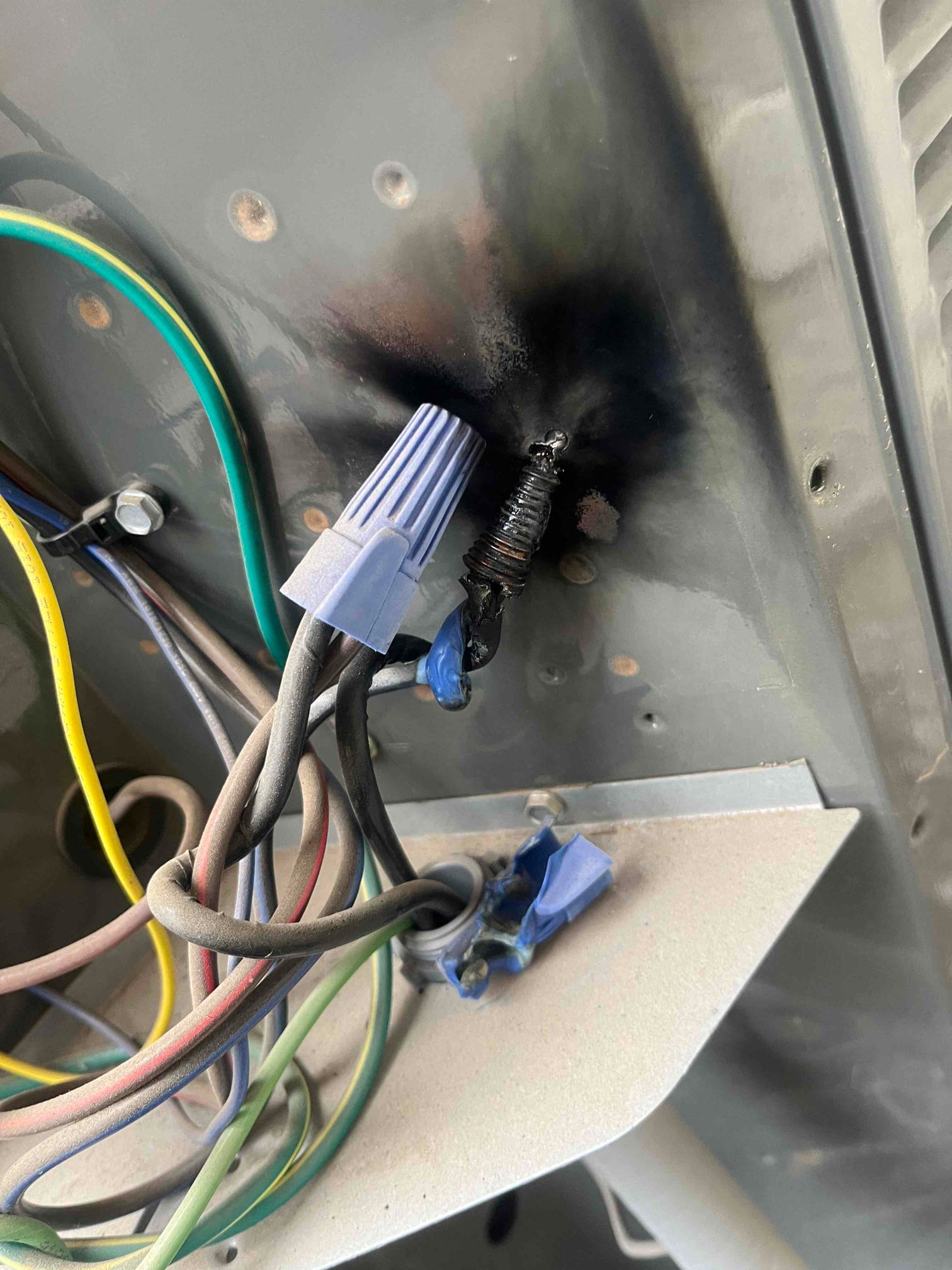 Charred wiring and blackened metal panel inside outdoor unit, with wire nuts and discolored conductors visible.