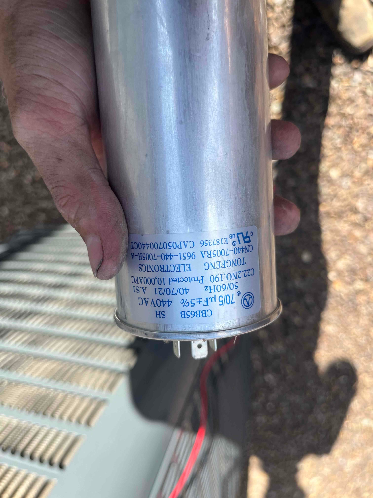 Dual-run capacitor labeled 70/5 μF ±5% 440VAC with three terminals visible, held beside the outdoor condenser.