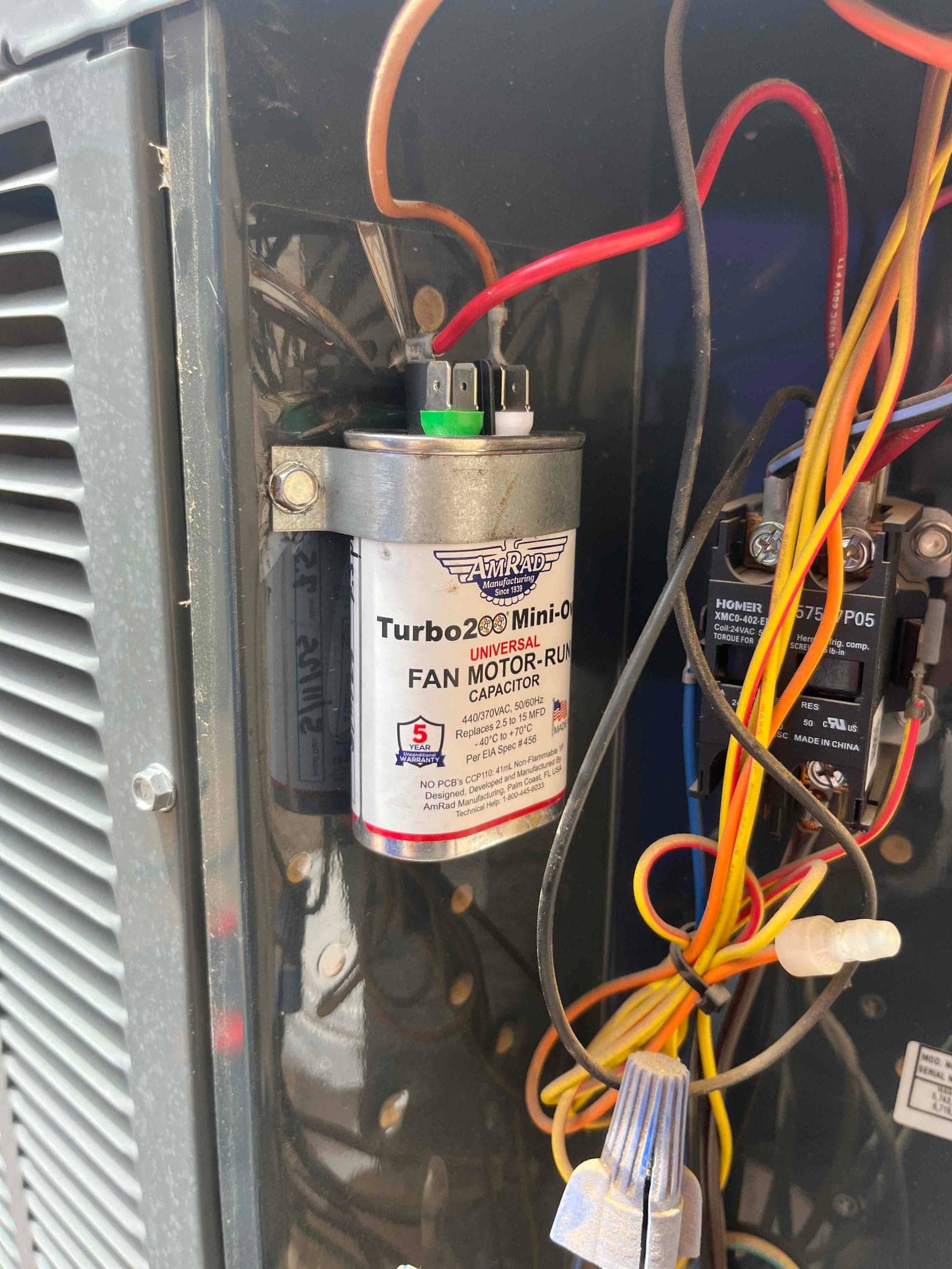 Fan motor run capacitor installed inside the outdoor condenser compartment, with wiring connected to its terminals and nearby contactor.