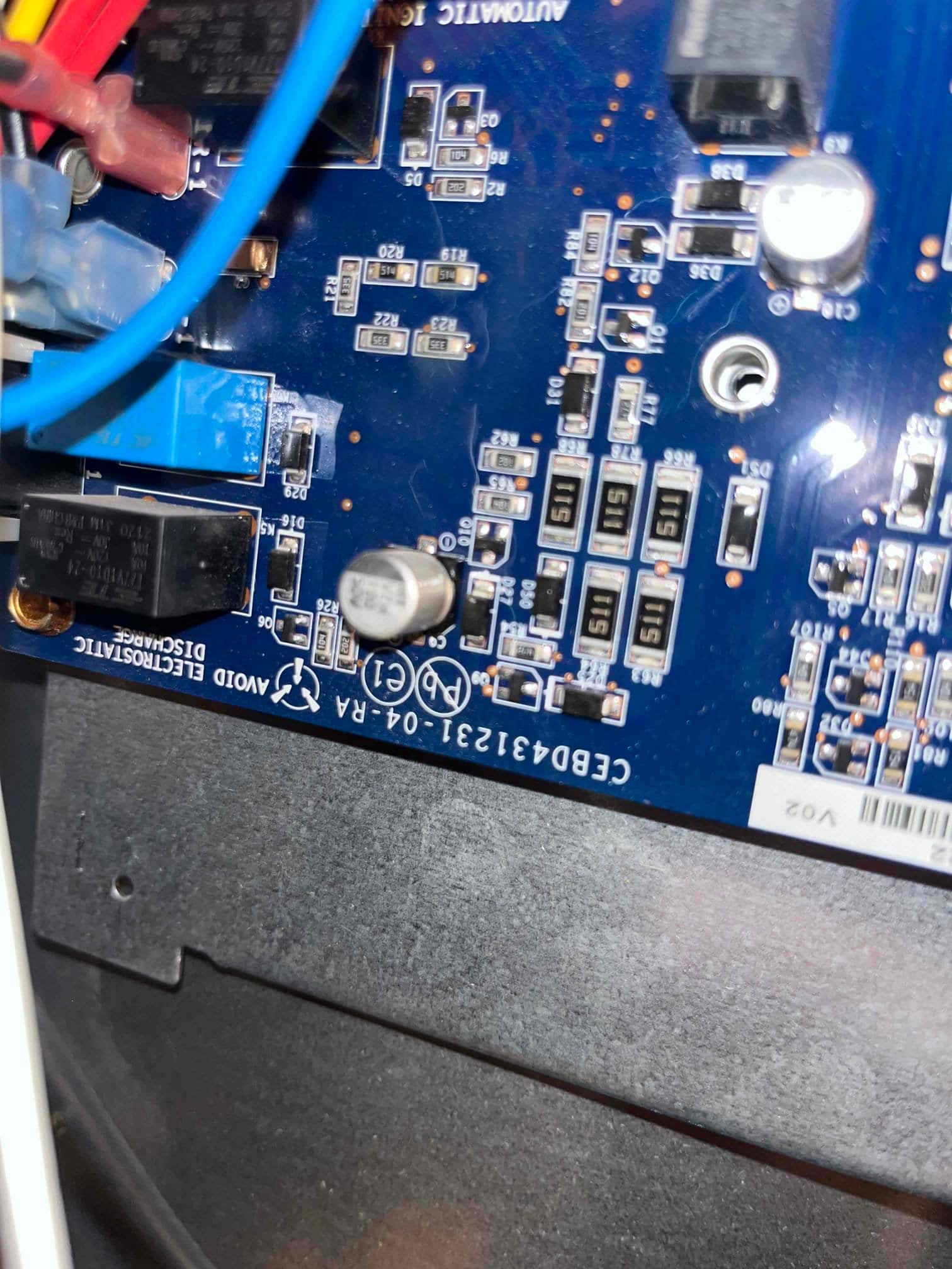 HVAC control board with relays, capacitors, surface-mount components, and connected wiring harnesses visible inside the unit.