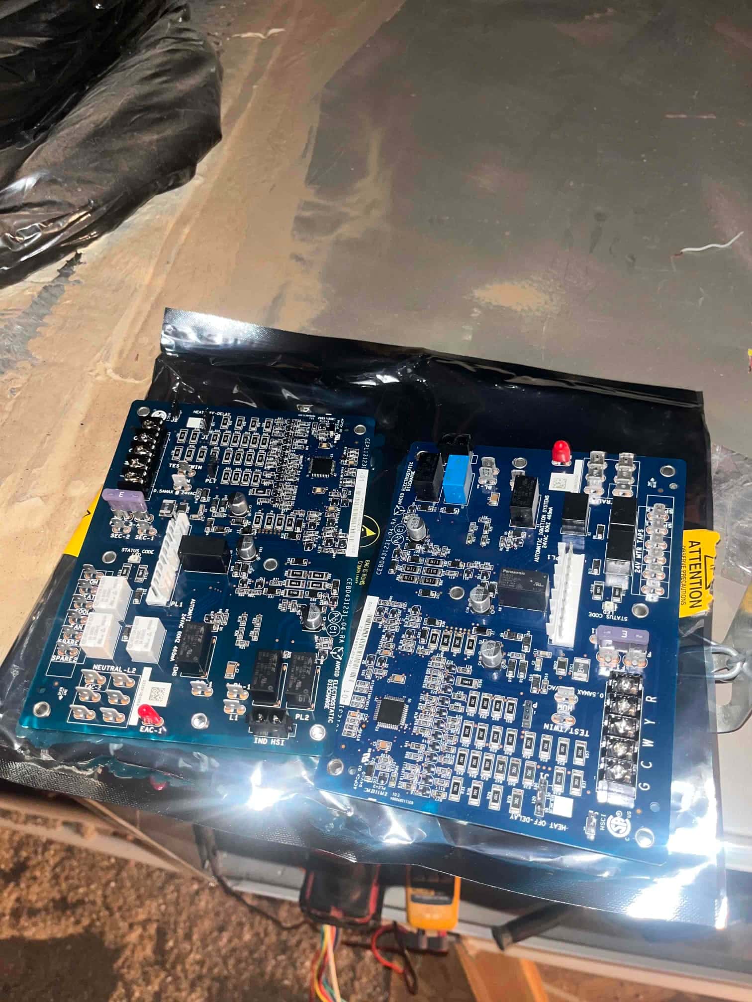 Two HVAC control boards rest on an anti-static bag, showing connectors and terminals labeled G, C, W, and R.
