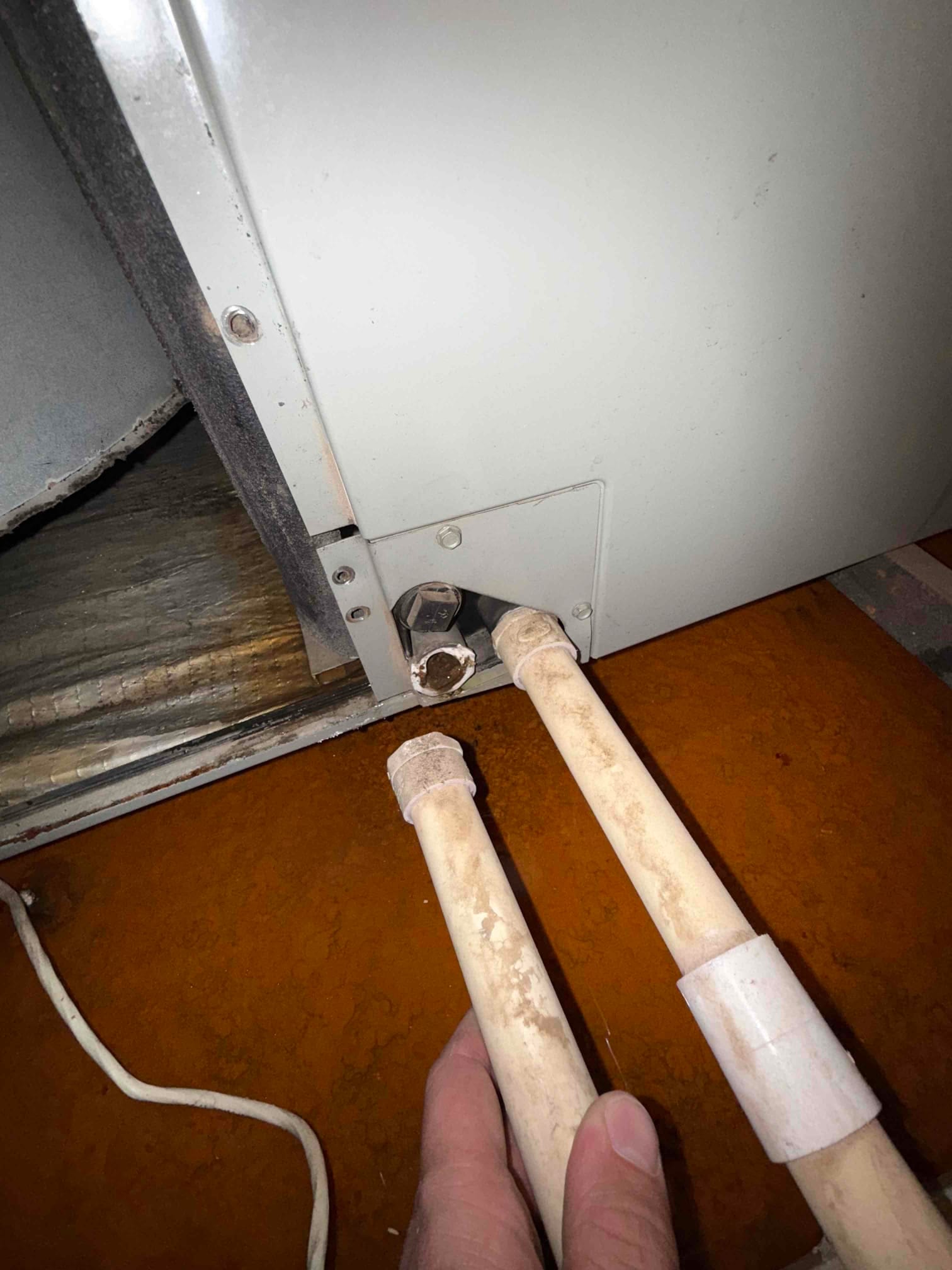 PVC drain pipes held near the air handler cabinet, with the condensate drain port open at the connection.
